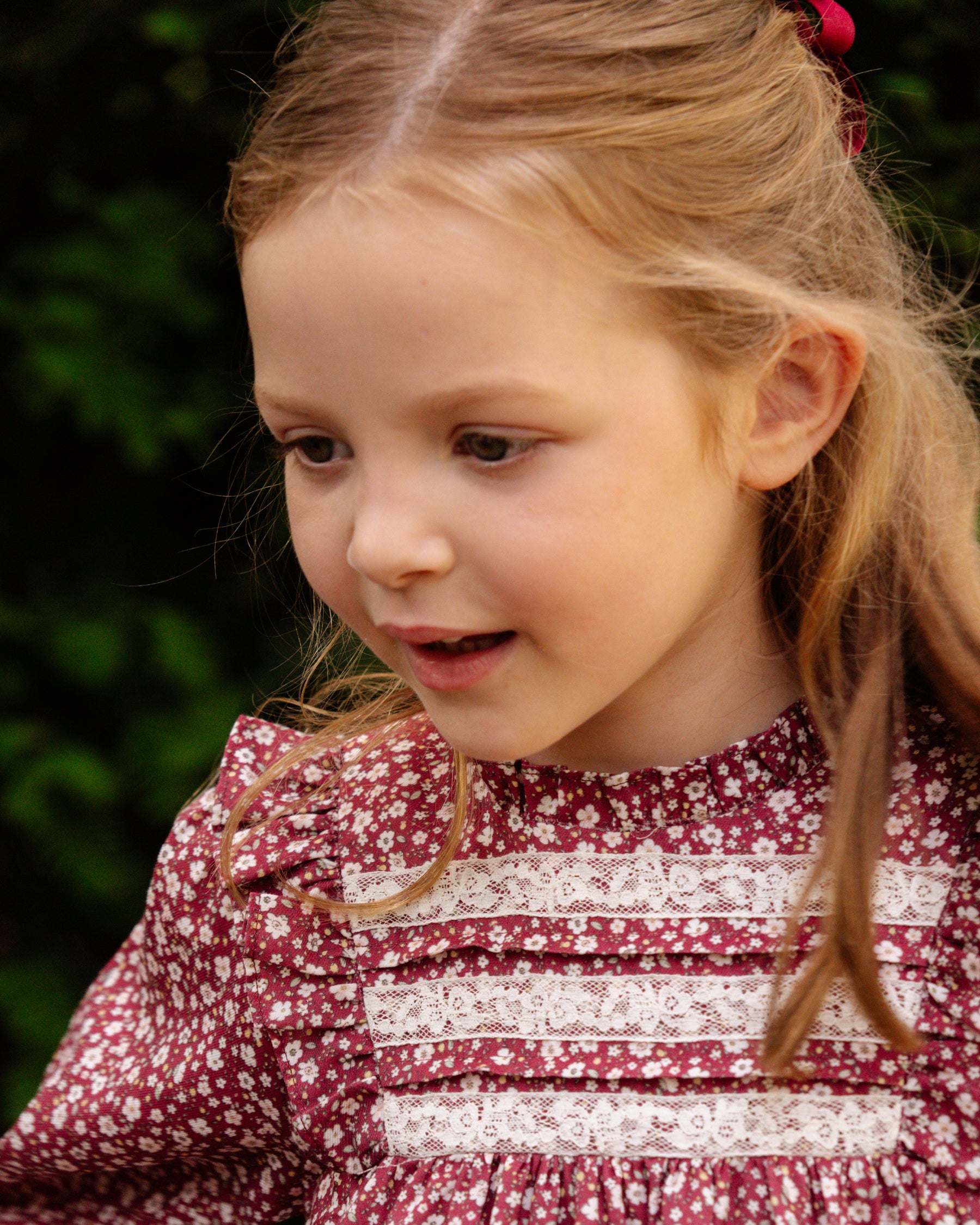 Young girl with blonde hair wearing a red and white patterned dress.