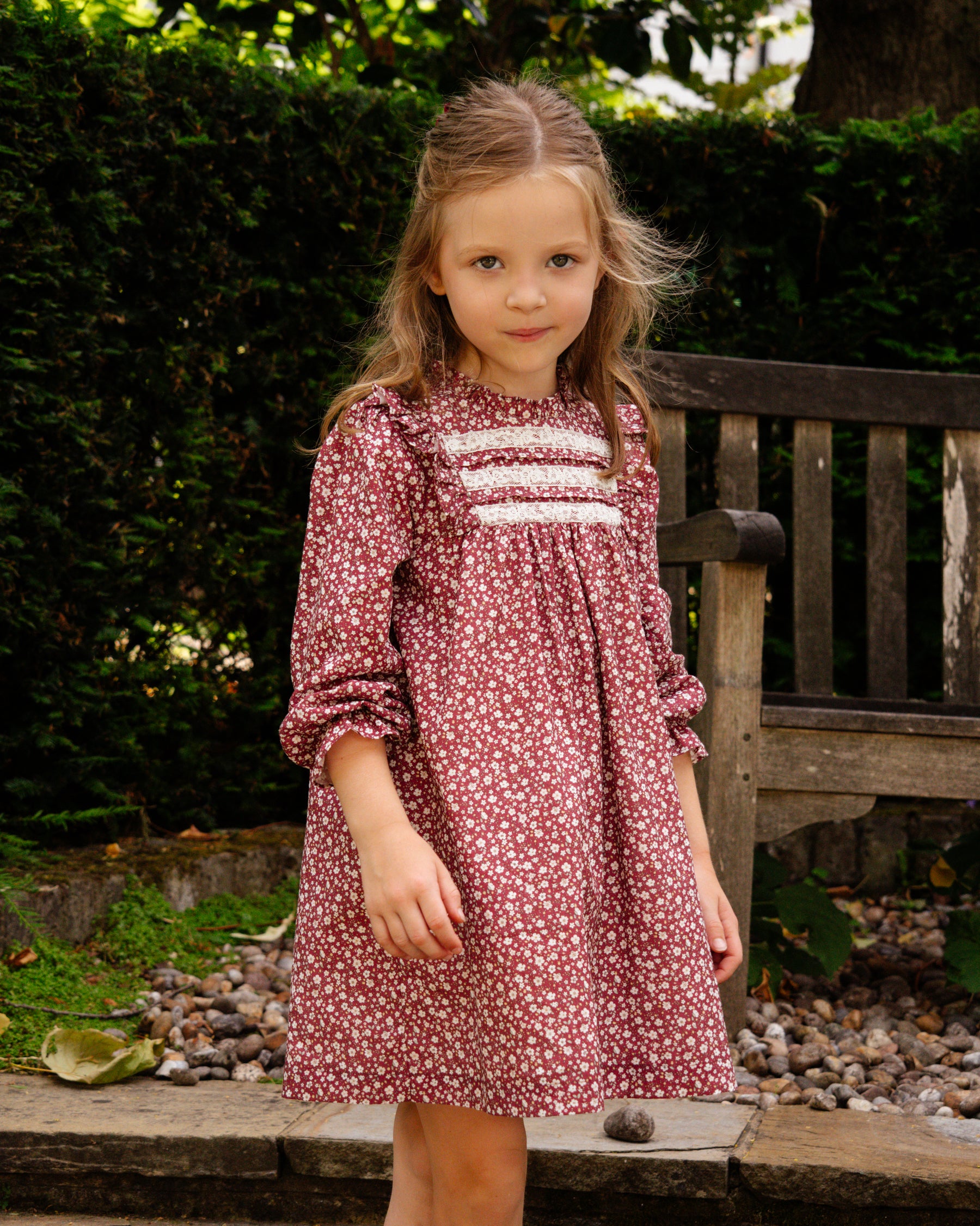 Young girl in a floral dress standing outdoors with greenery in the background