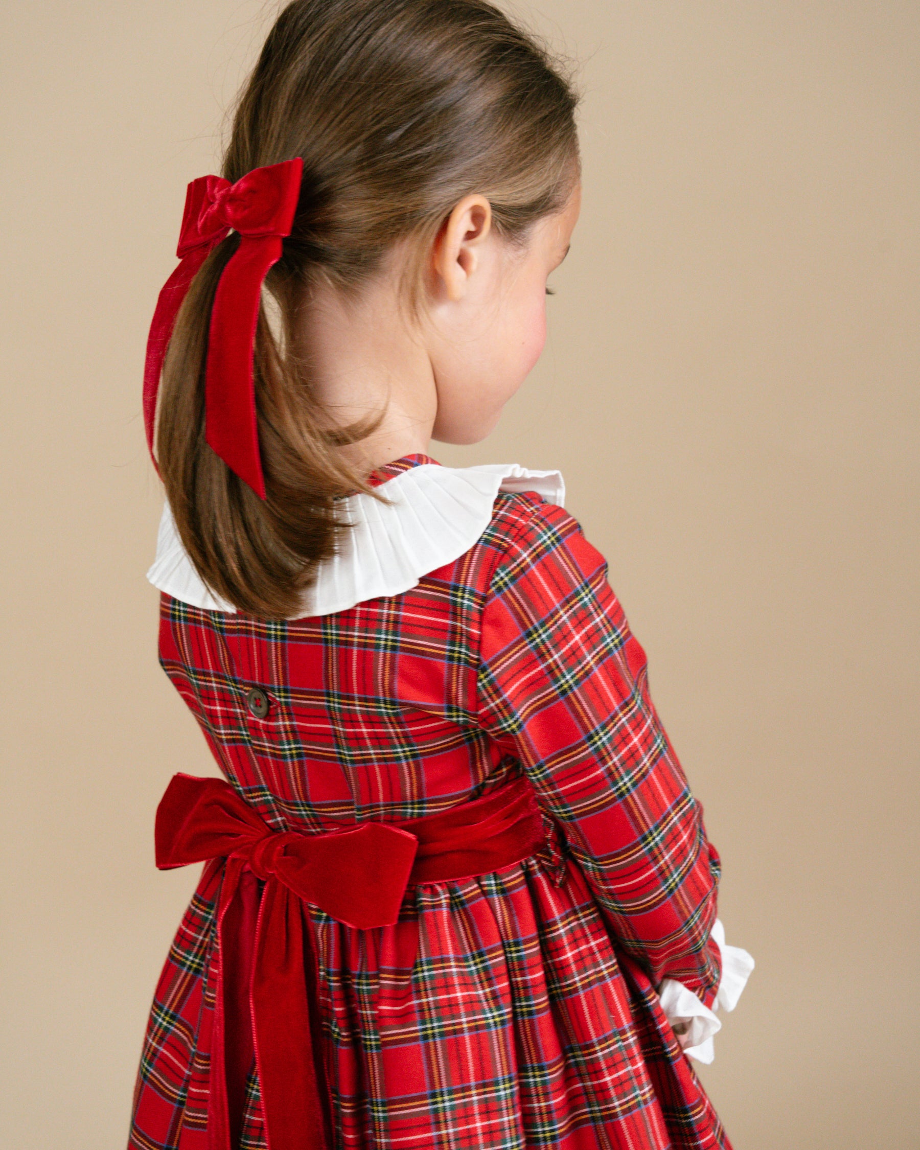 Child wearing a red plaid dress with a large bow on a beige background
