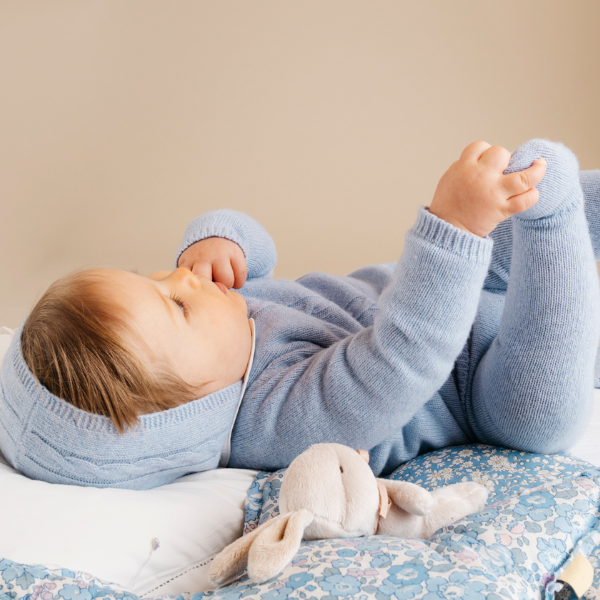 Baby in a blue outfit lying on a bed with a toy