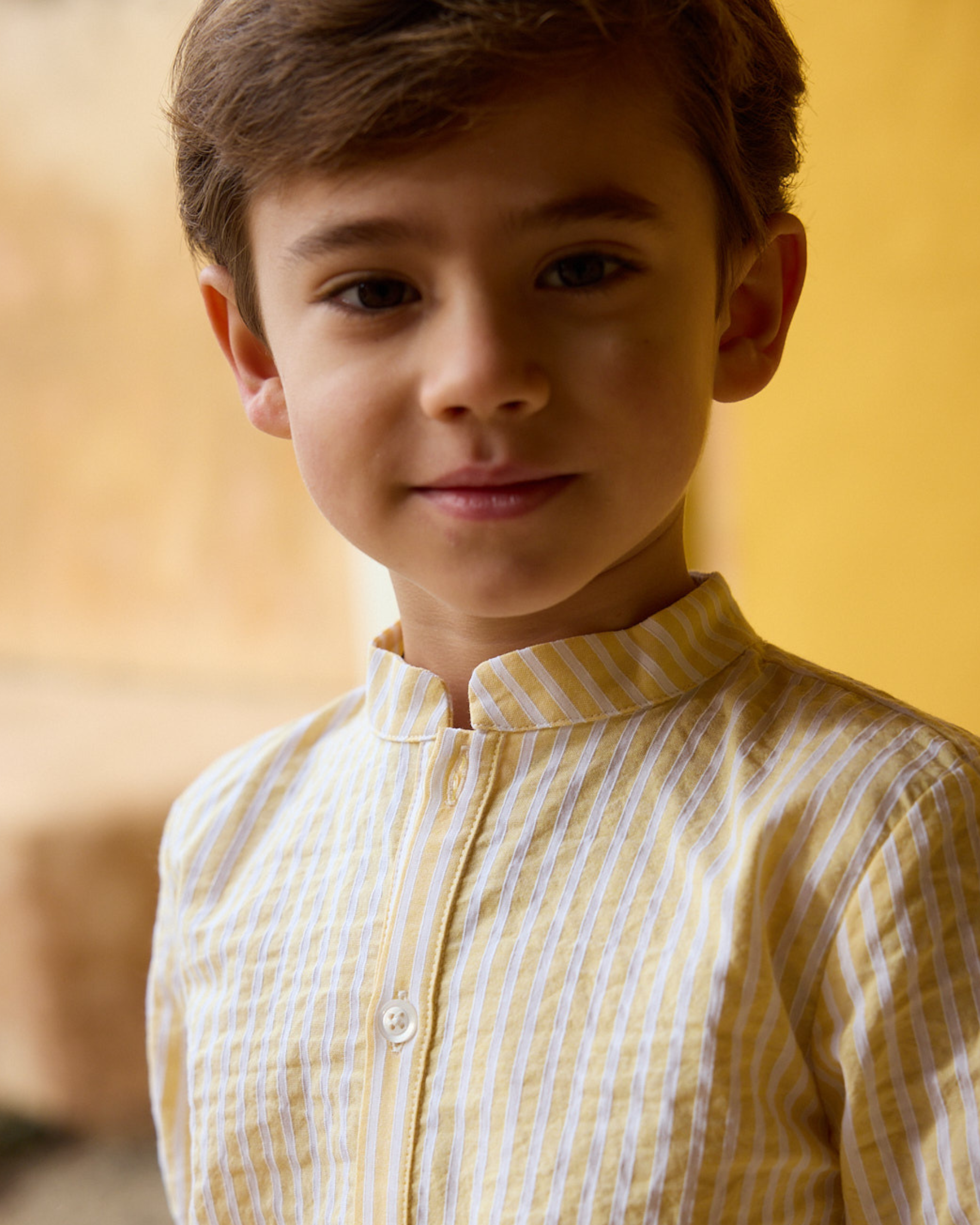 Young boy wearing a yellow and white striped shirt against a blurred background