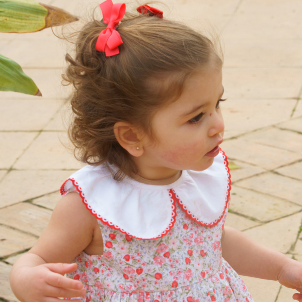 Young girl wearing a floral dress with a white collar and red trim, standing on a paved surface.