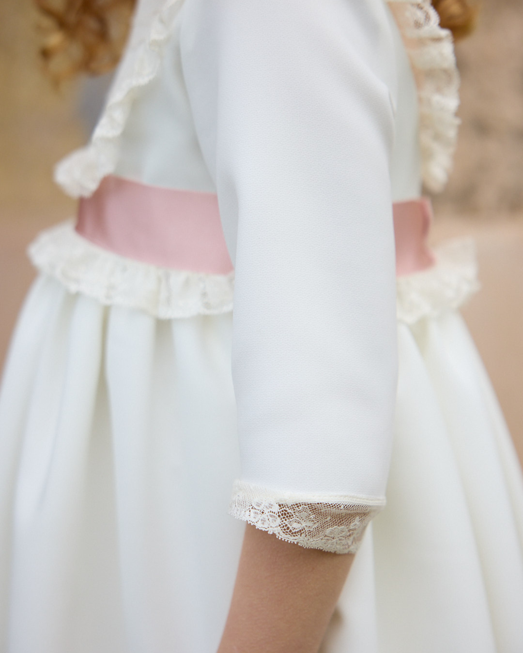 White dress with pink sash and lace details on a blurred background