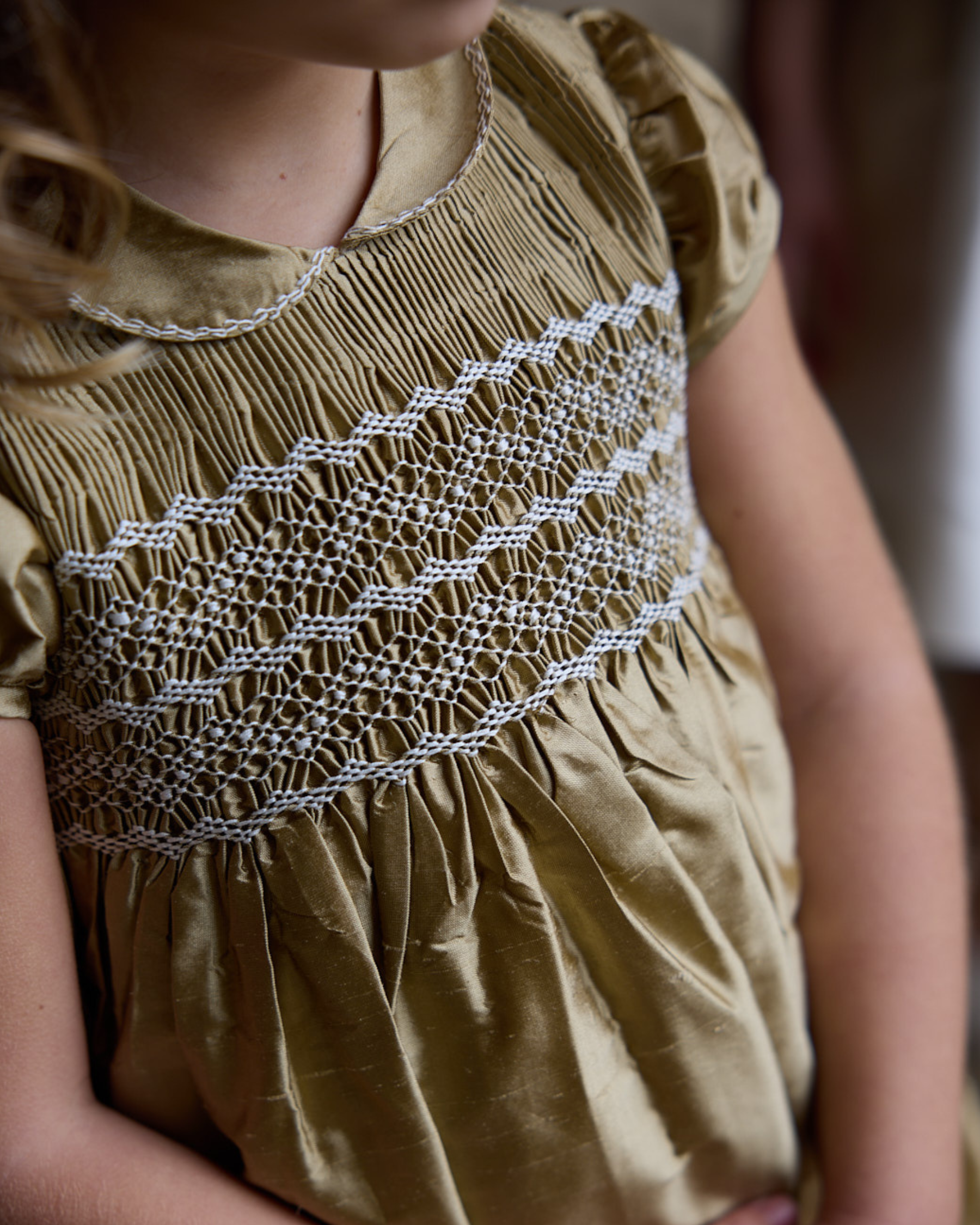 Close-up of a child wearing a beige dress with intricate white lace detailing.