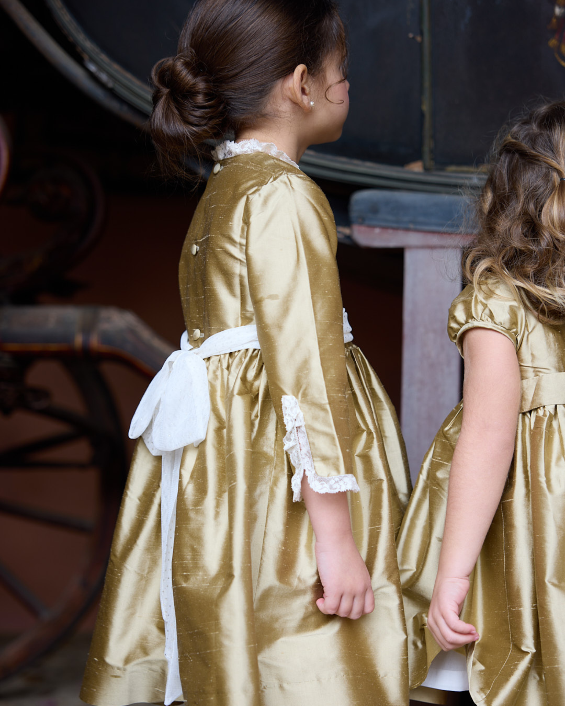 Two children in gold dresses standing close to each other.