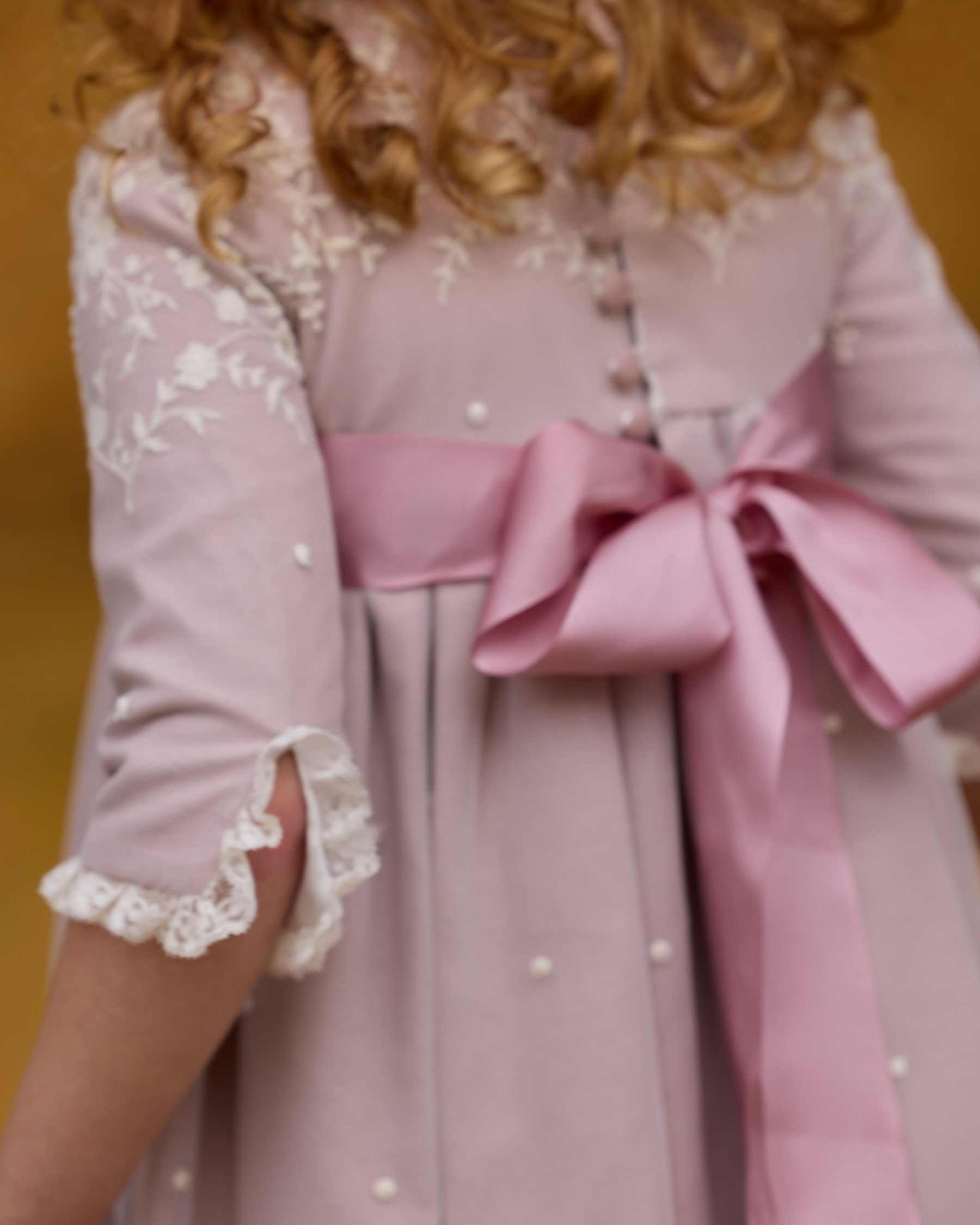 Pink dress with lace details and a large bow on a blurred background