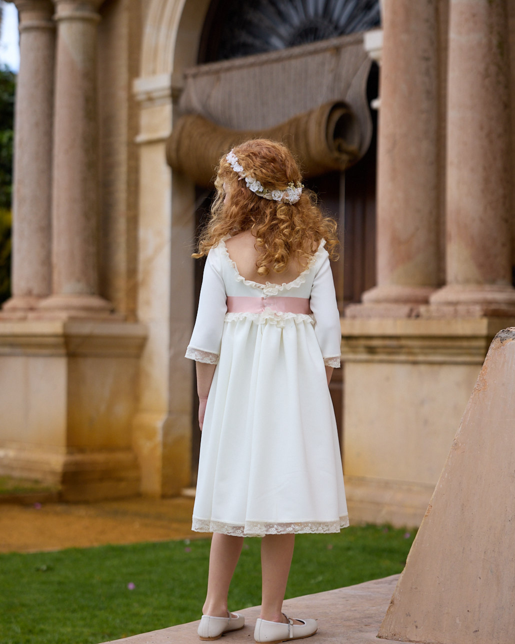 Young girl in a white dress with a pink belt standing in front of classical architecture.