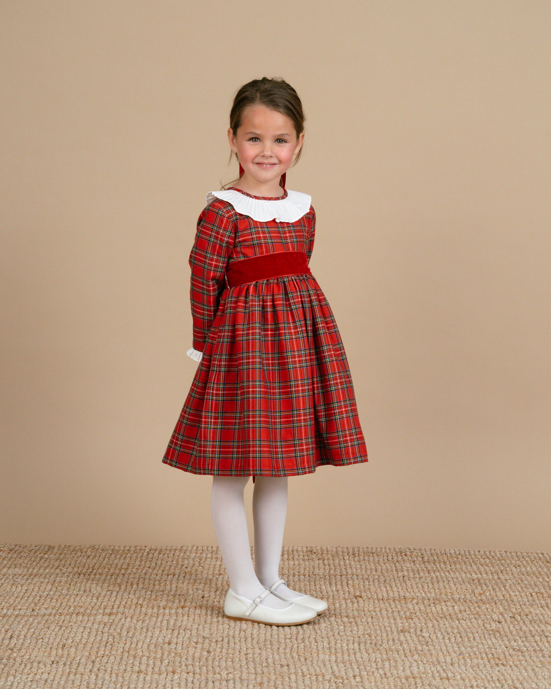 Young girl wearing a red plaid dress with a white collar against a beige background