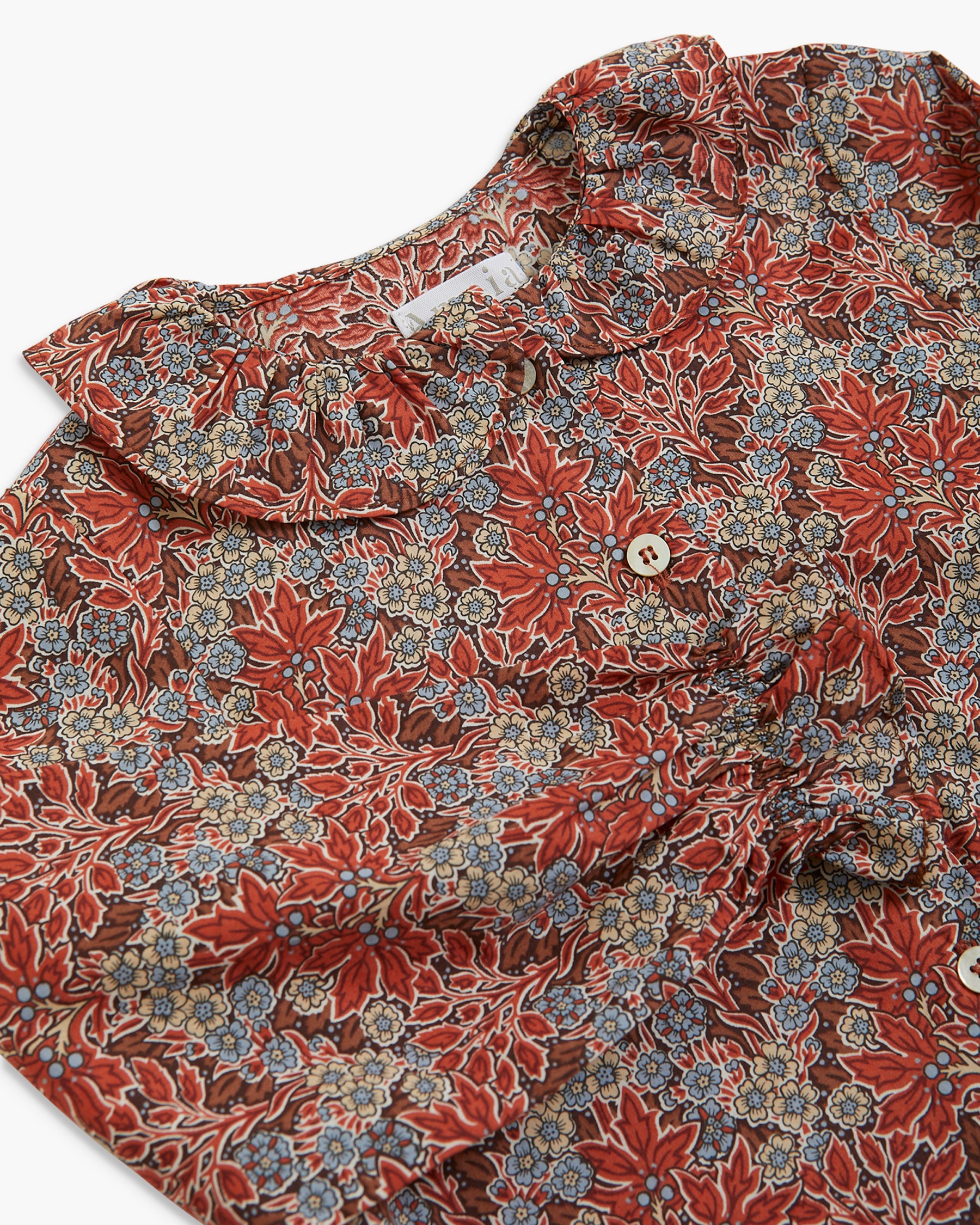 A close-up of a ruffled blouse with a dense floral and botanical print in rust red, dusty blue, and beige, featuring a buttoned front.