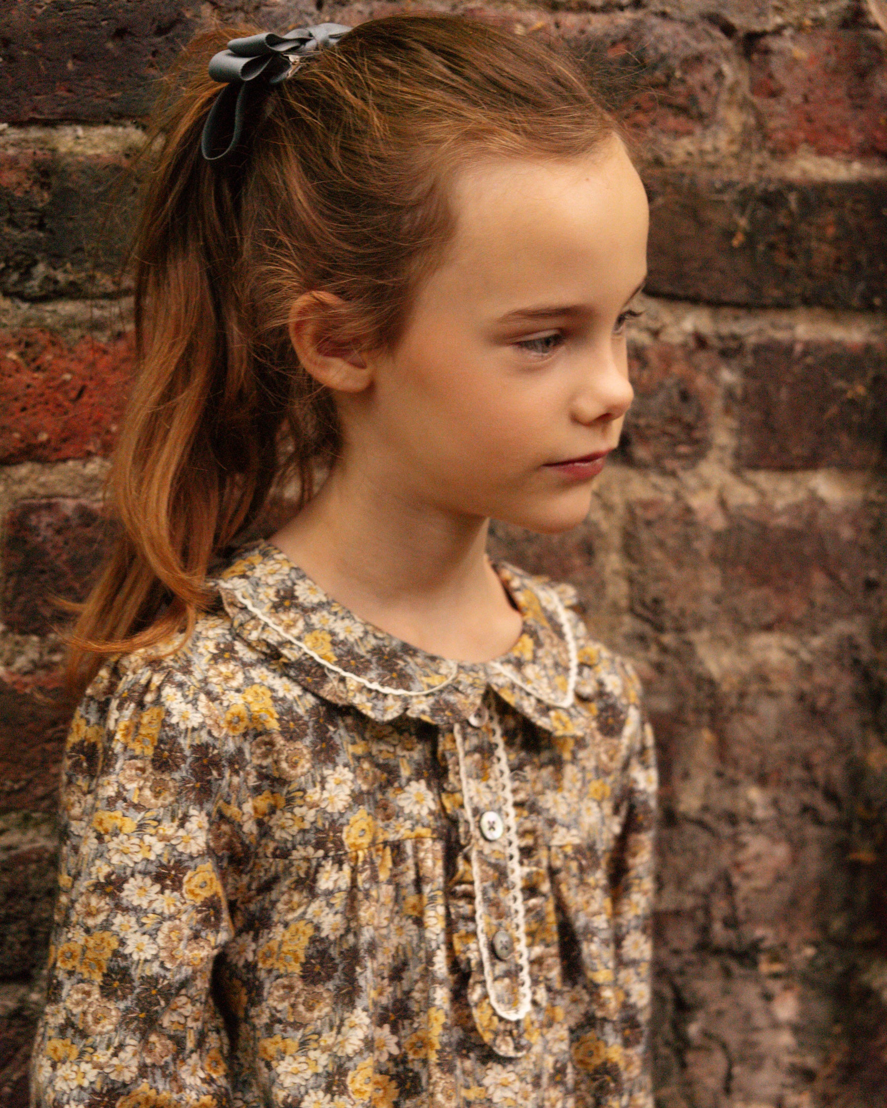 Young girl wearing a floral blouse against a brick wall