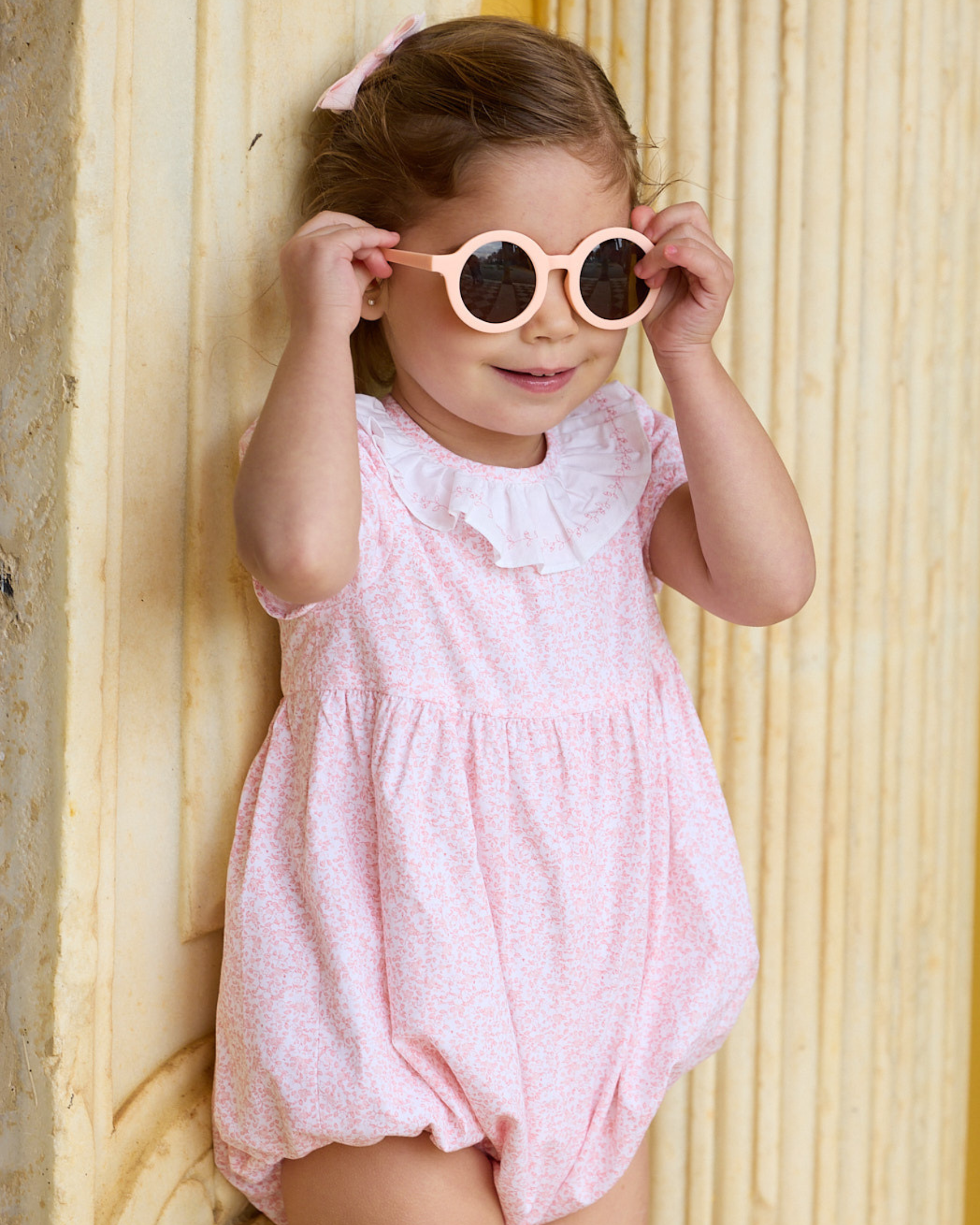 Child wearing a pink outfit and sunglasses against a wooden background