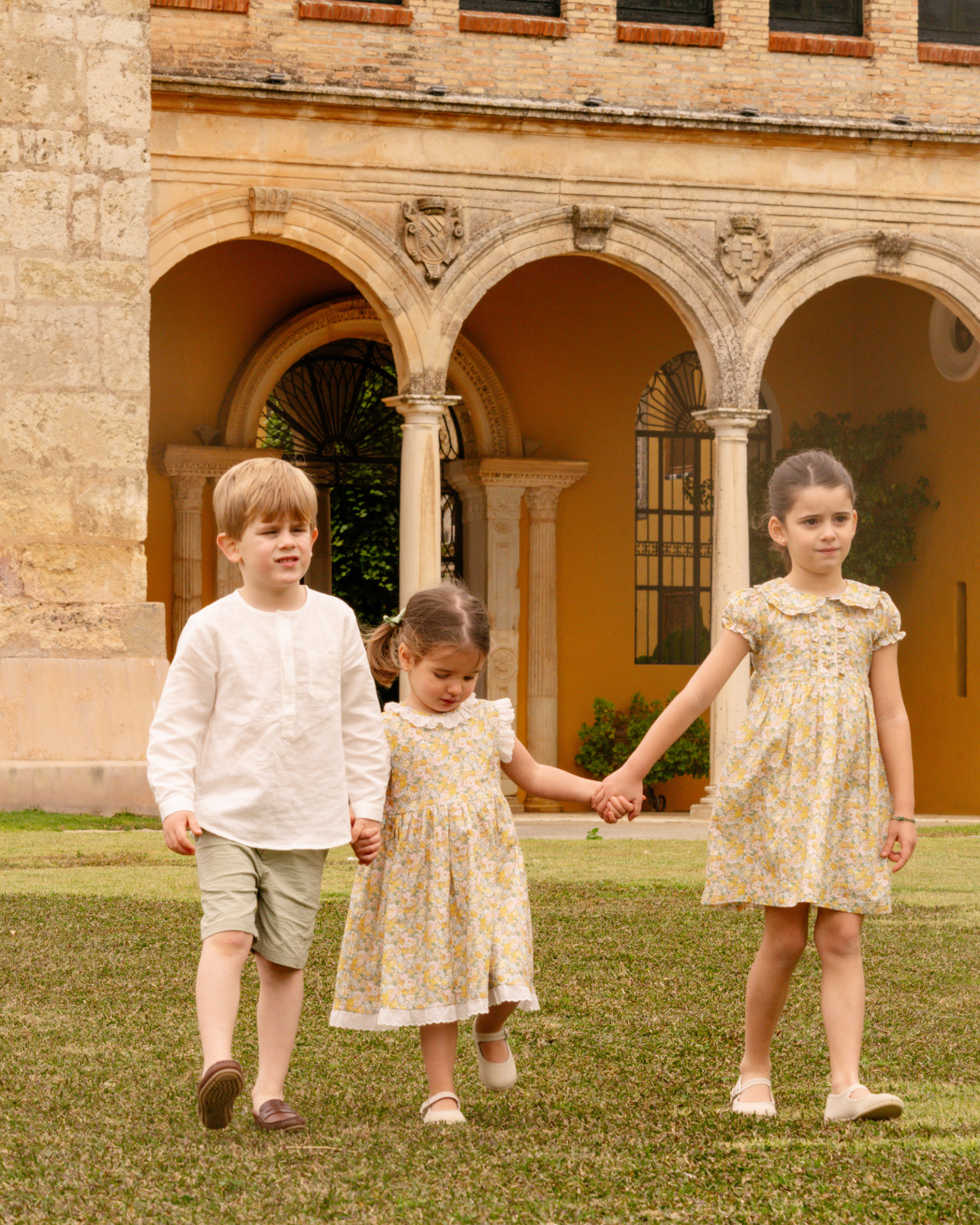 Three children holding hands in a courtyard with classical architecture
