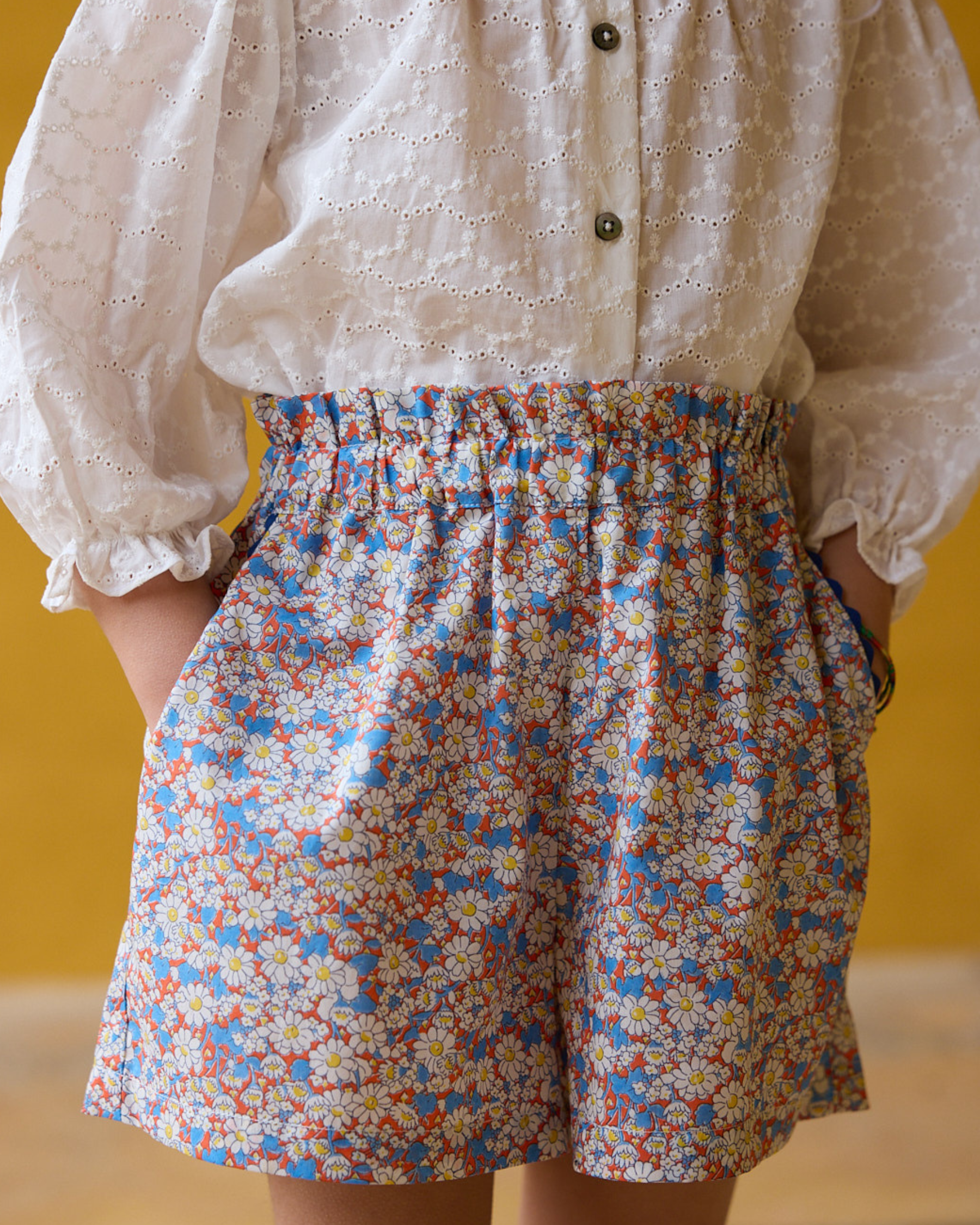 Girl wearing a white blouse with puffed sleeves and colorful floral shorts against a yellow background