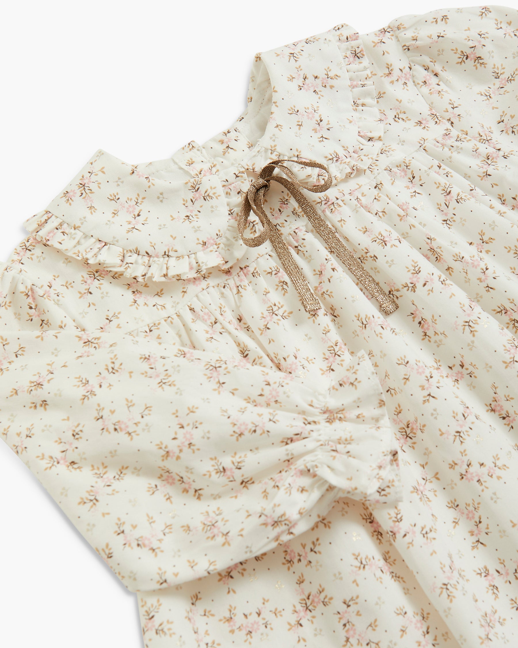 Close-up of a cream-colored baby dress with a delicate brown floral print, featuring a ruffled collar and a matching fabric bow at the neckline.