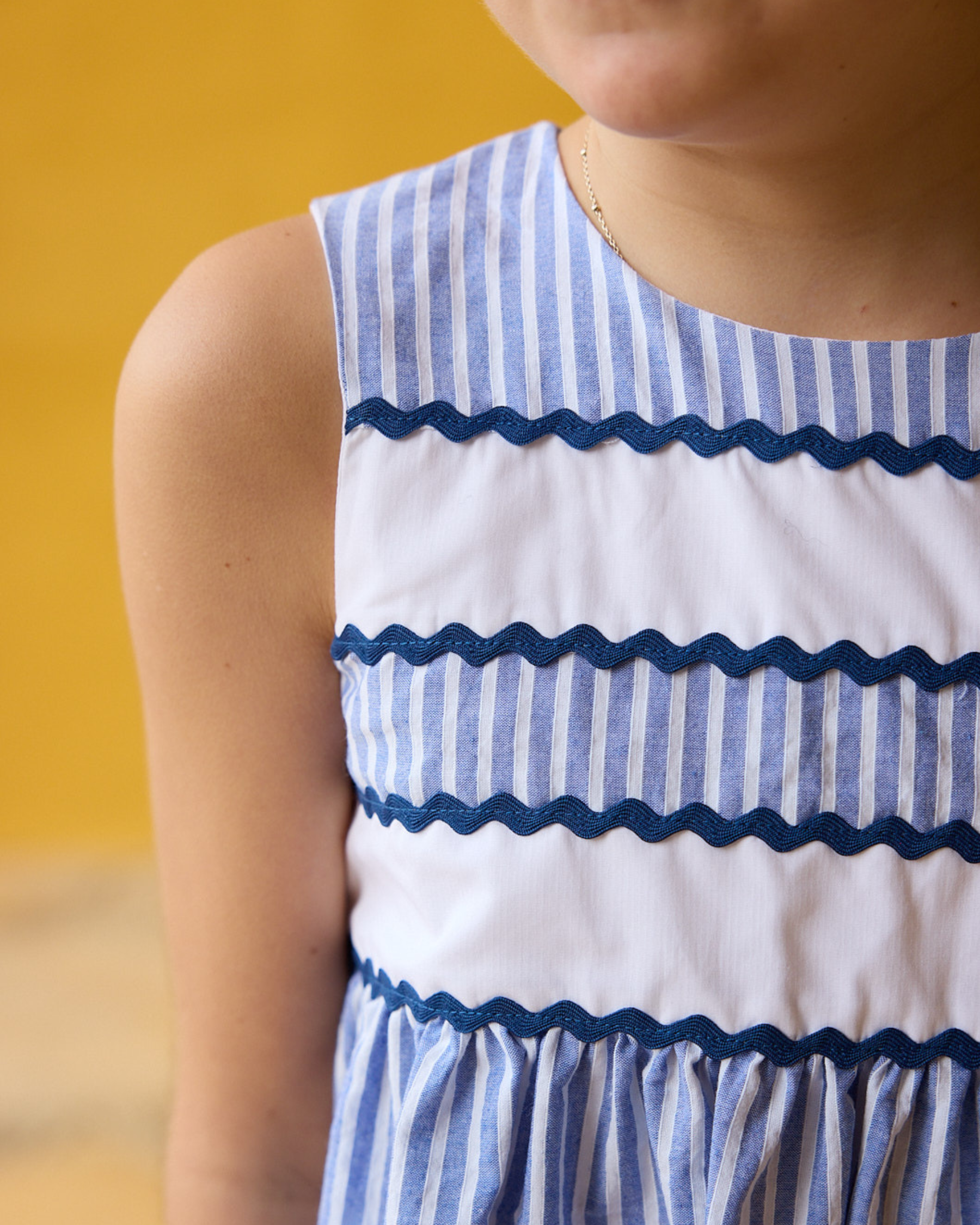 Close-up of a child wearing a blue and white striped dress against a yellow background