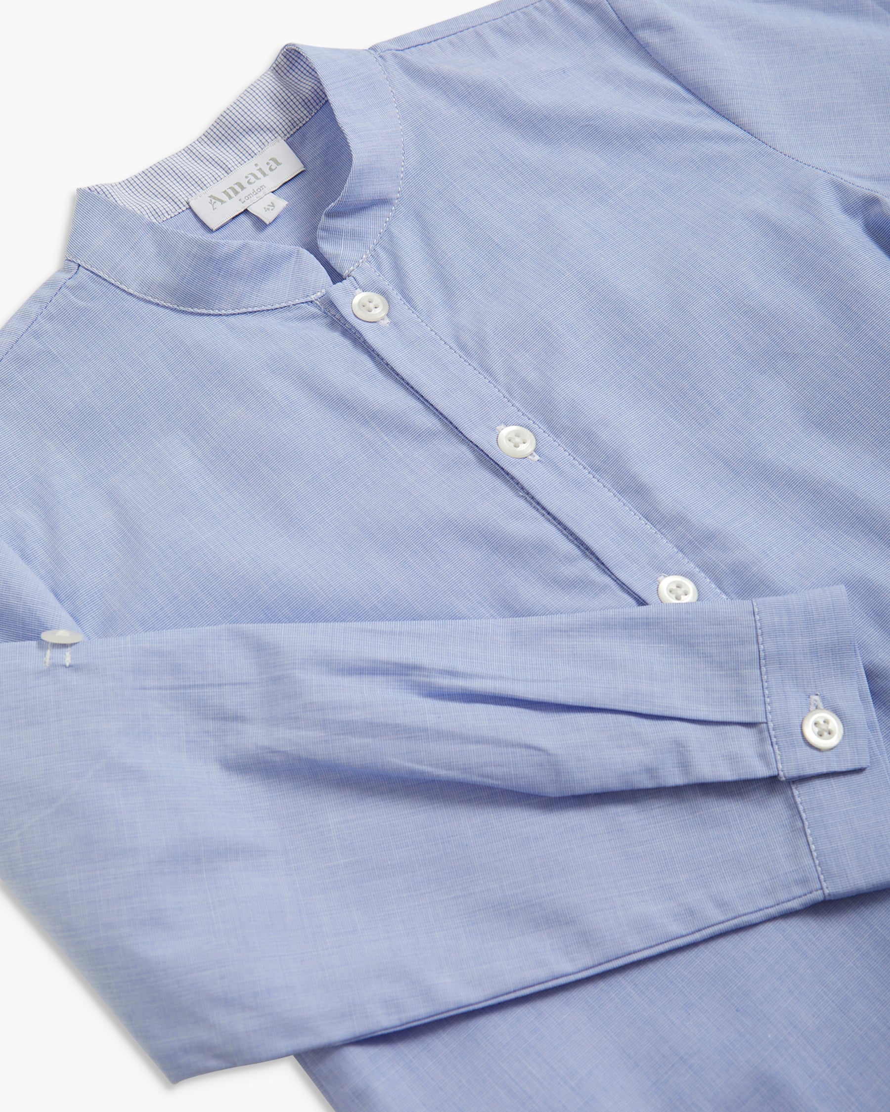 A close-up of a light blue long-sleeve button-up shirt with a band collar and white buttons, laid flat on a white background.