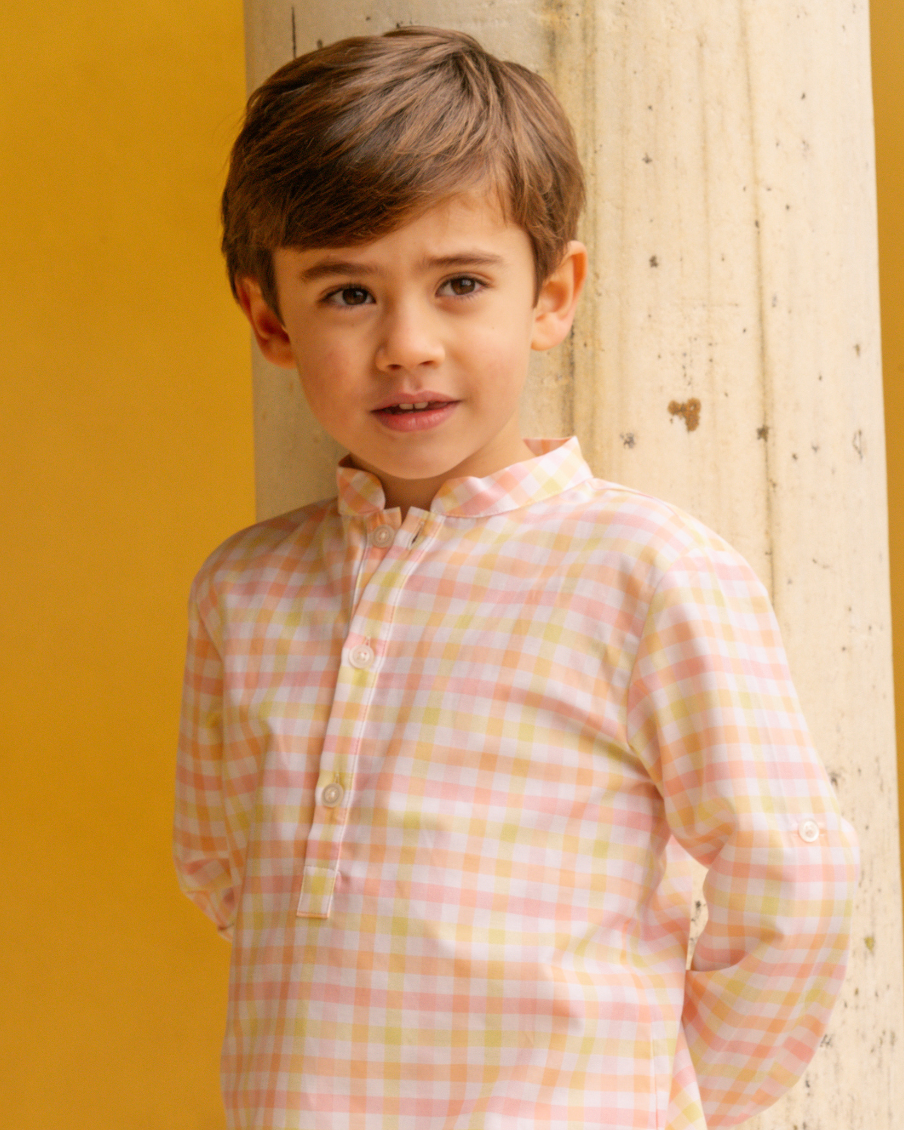 Young boy wearing a checkered shirt against a yellow wall