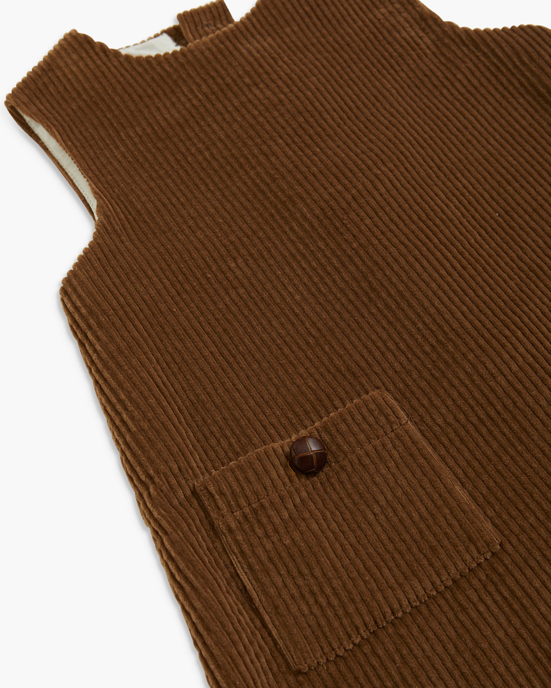 Close-up of a brown ribbed corduroy garment, likely a sleeveless top or romper, with a chest pocket and a single dark button, shown on a white background.