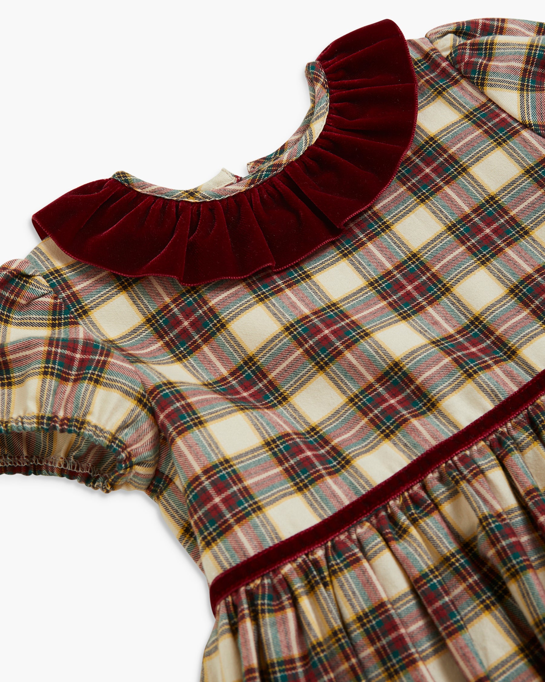 A close-up of a children's dress featuring a cream, green, and red plaid pattern, a deep burgundy velvet ruffled collar, and a matching burgundy velvet waistband.