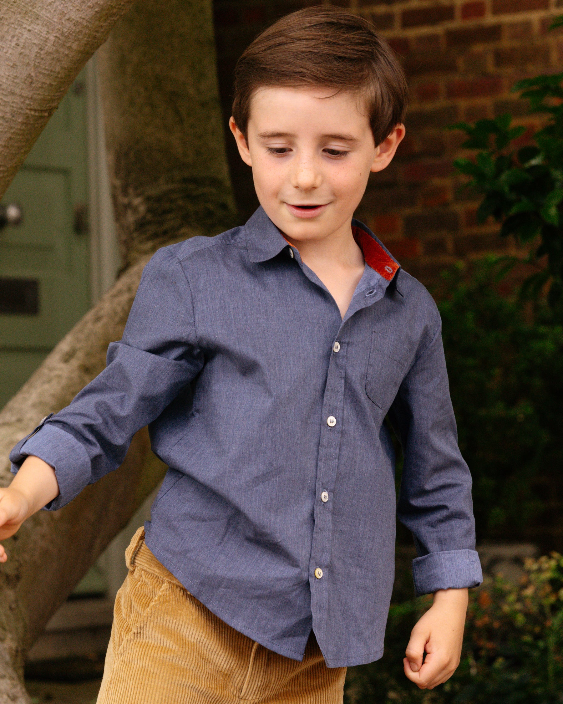 Young boy wearing a blue shirt with a red collar outdoors.