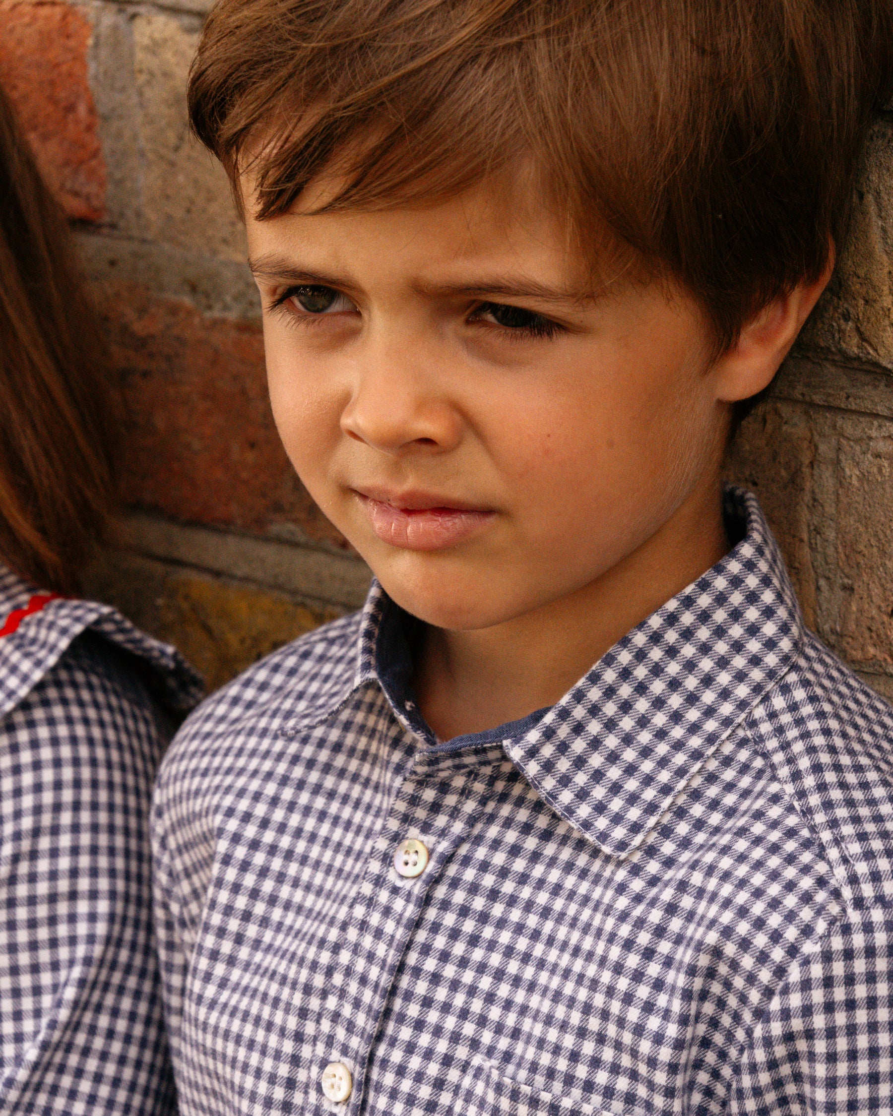 Child wearing a blue checkered shirt against a brick wall