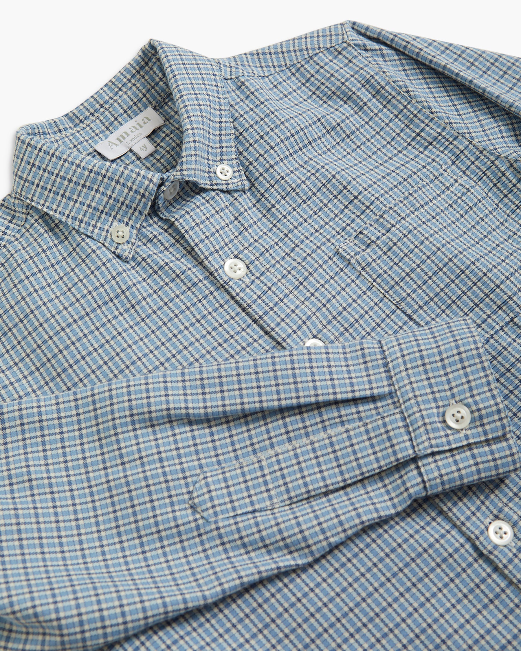 A close-up of a long-sleeve button-down shirt with a fine blue and white checkered pattern, featuring a pointed collar and white buttons.
