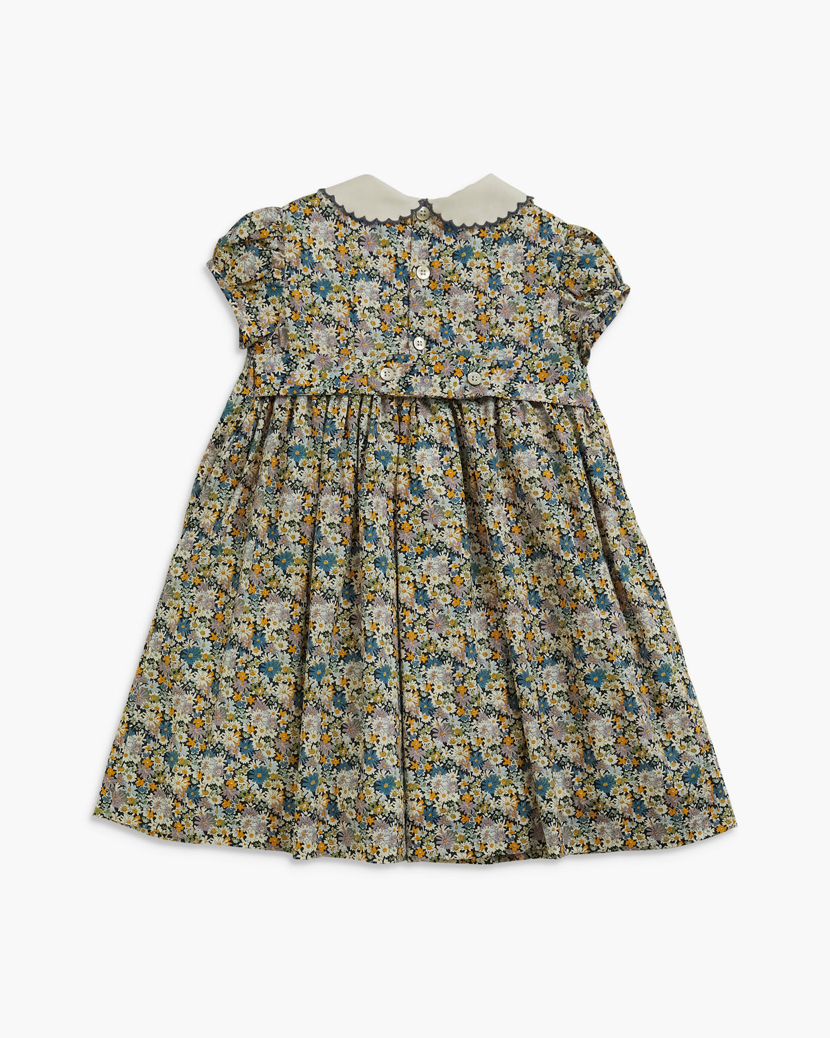 A toddler girl's short-sleeve dress with a dense floral print in muted blue, yellow, and green tones on a light beige base. It features a white Peter Pan collar and a buttoned bodice, shown against a plain light gray background.