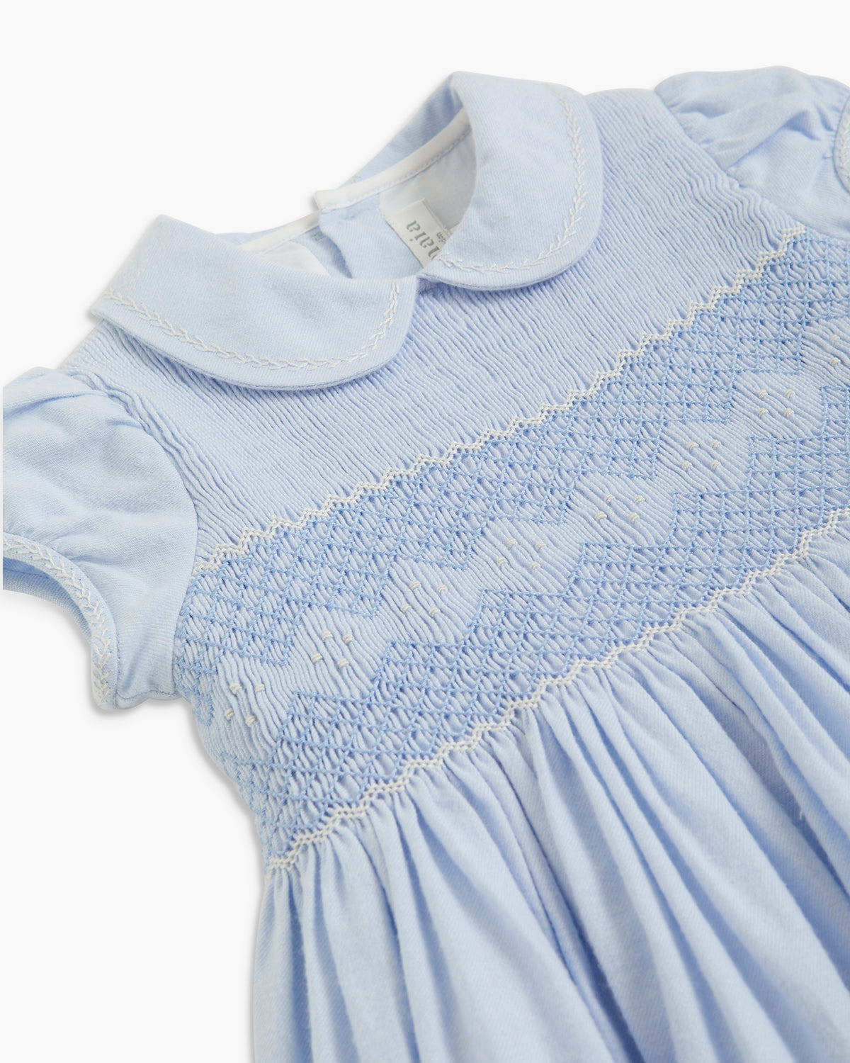 Close-up of a light blue baby dress featuring a smocked bodice with a diamond pattern, a white Peter Pan collar, and short puff sleeves.