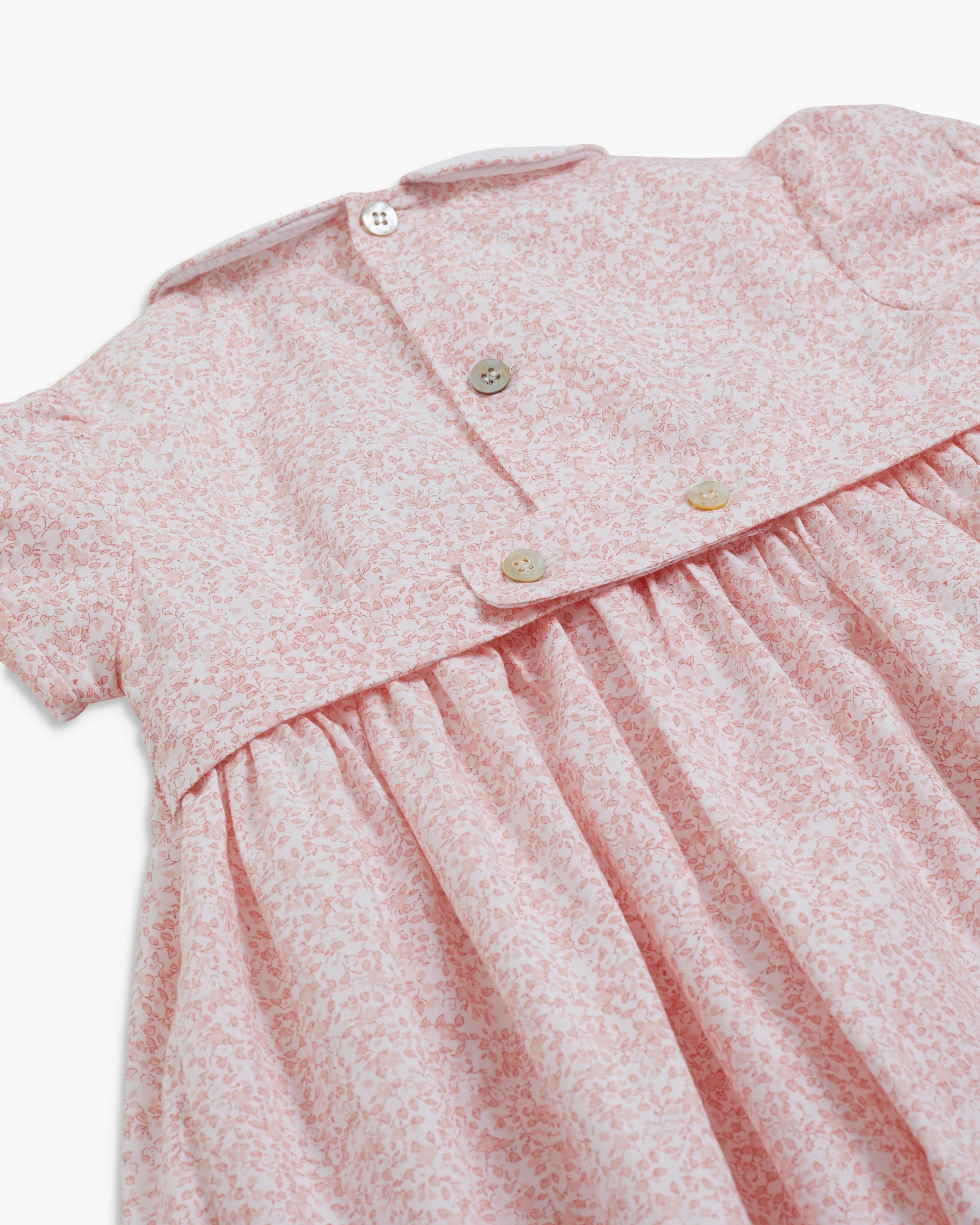 Close-up of a pink baby dress with buttons on a white background