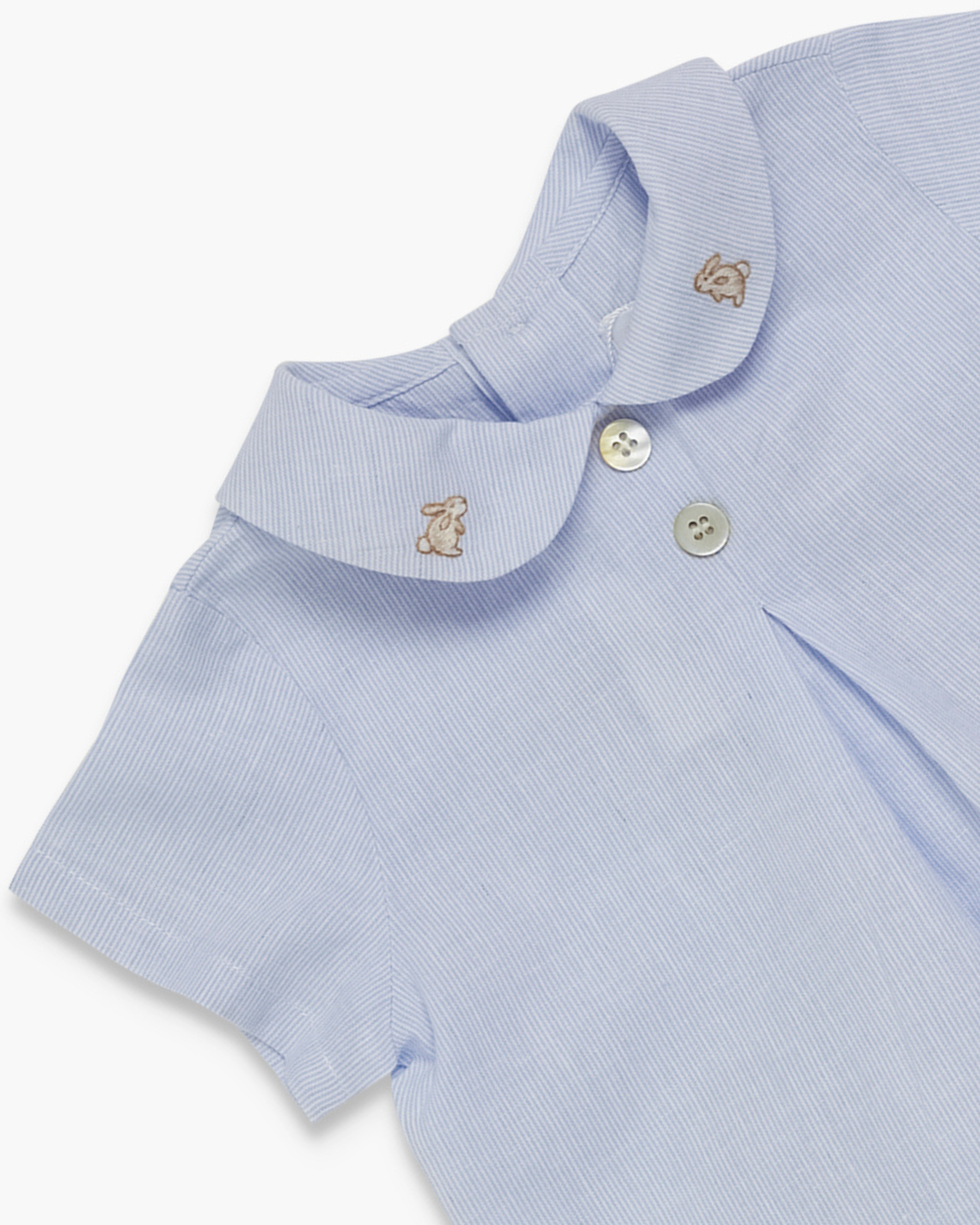 Close-up of a light blue baby outfit with embroidered bunny details on a white background