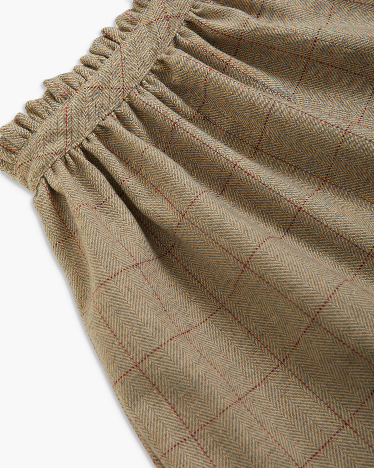Close-up of a herringbone-patterned fabric with a gathered elastic waistband, in a muted taupe-beige color with thin red windowpane lines.