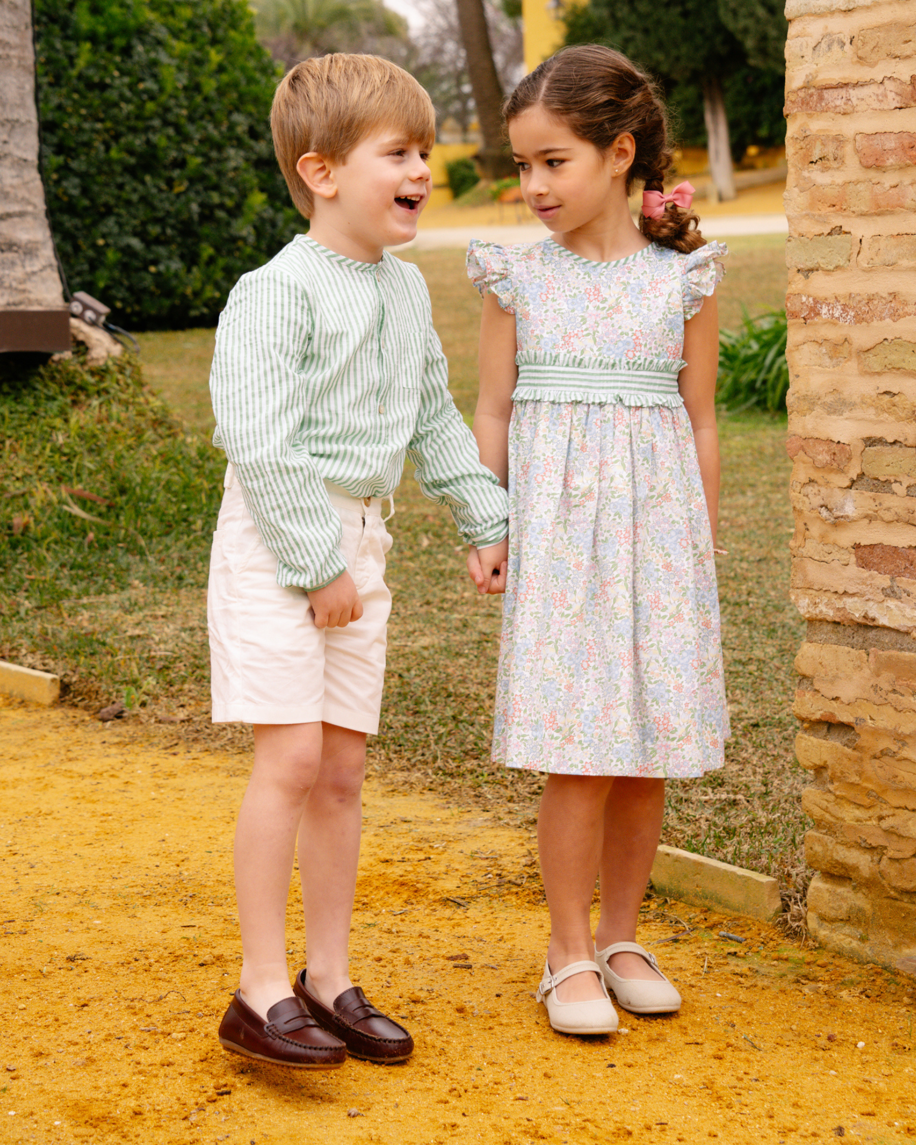 Two children, a boy and a girl, standing outdoors on a sunny day.