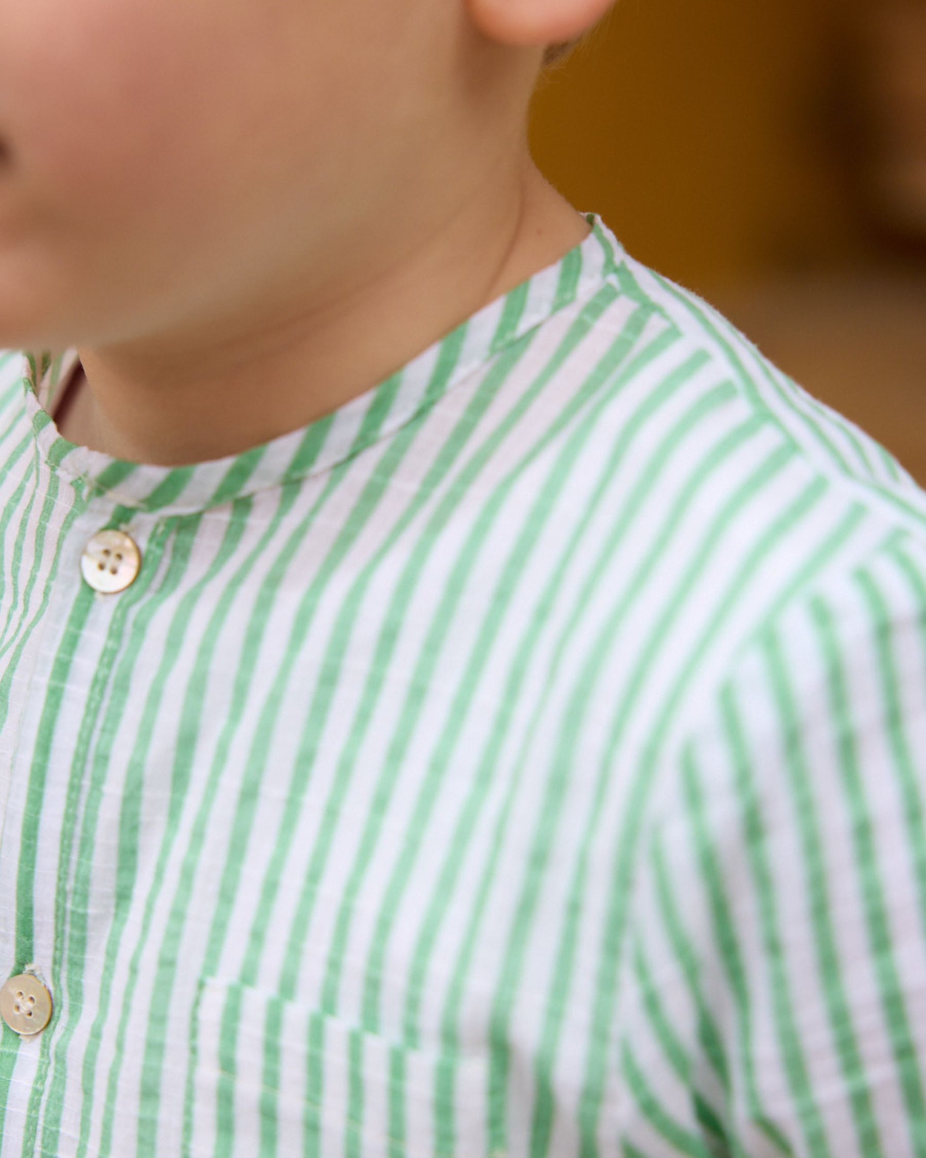 Close-up of a child wearing a green and white striped shirt with a blurred background