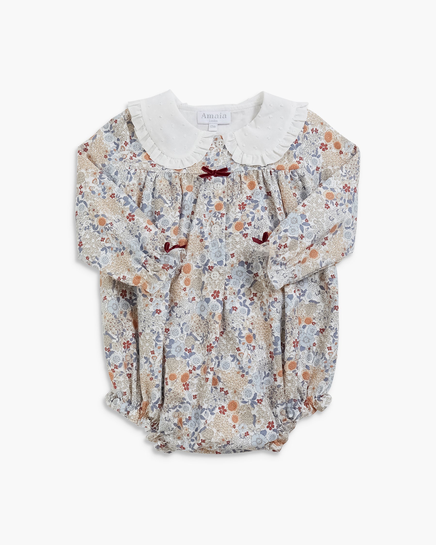 A baby long-sleeve romper with a delicate floral print in beige, blue, and brown, featuring a contrasting white ruffled Peter Pan collar and small dark red bow accents.