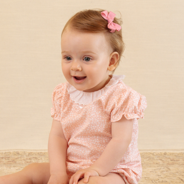 Baby wearing a pink dress with ruffled sleeves against a beige background