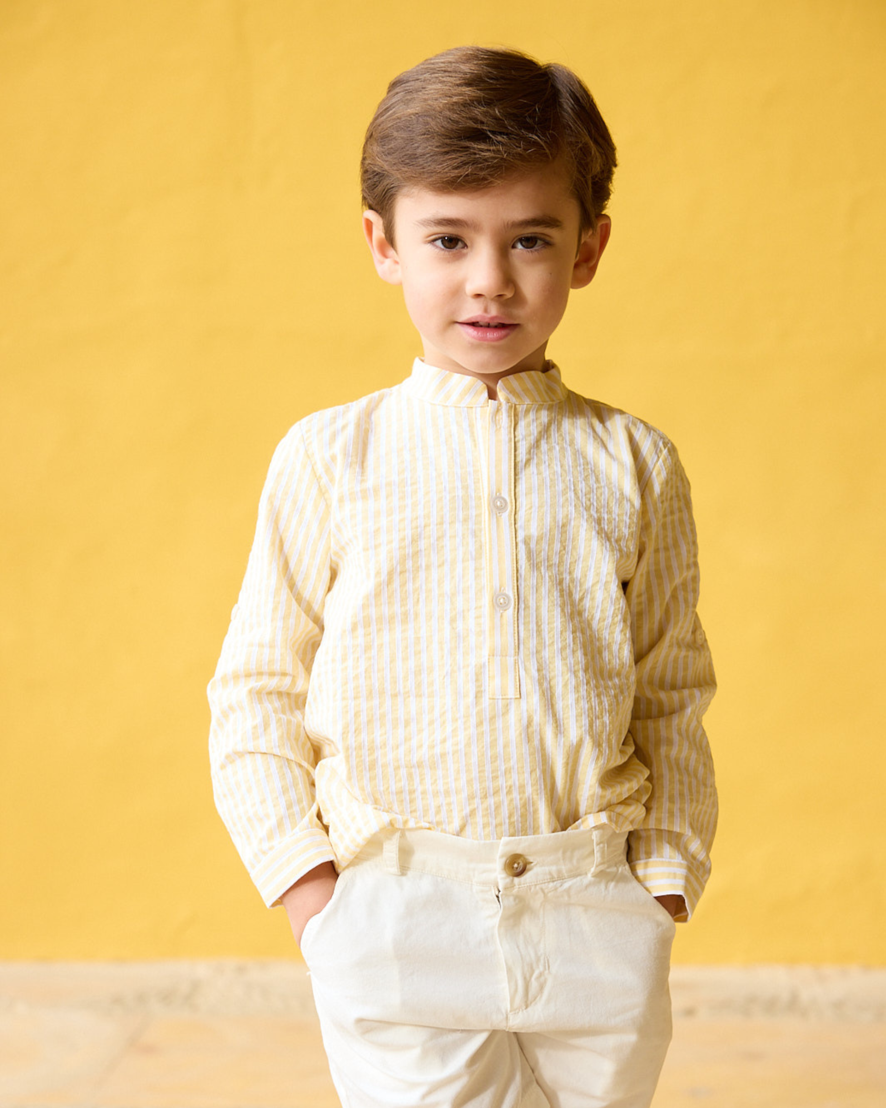 Young boy wearing a light-colored shirt and pants against a yellow background