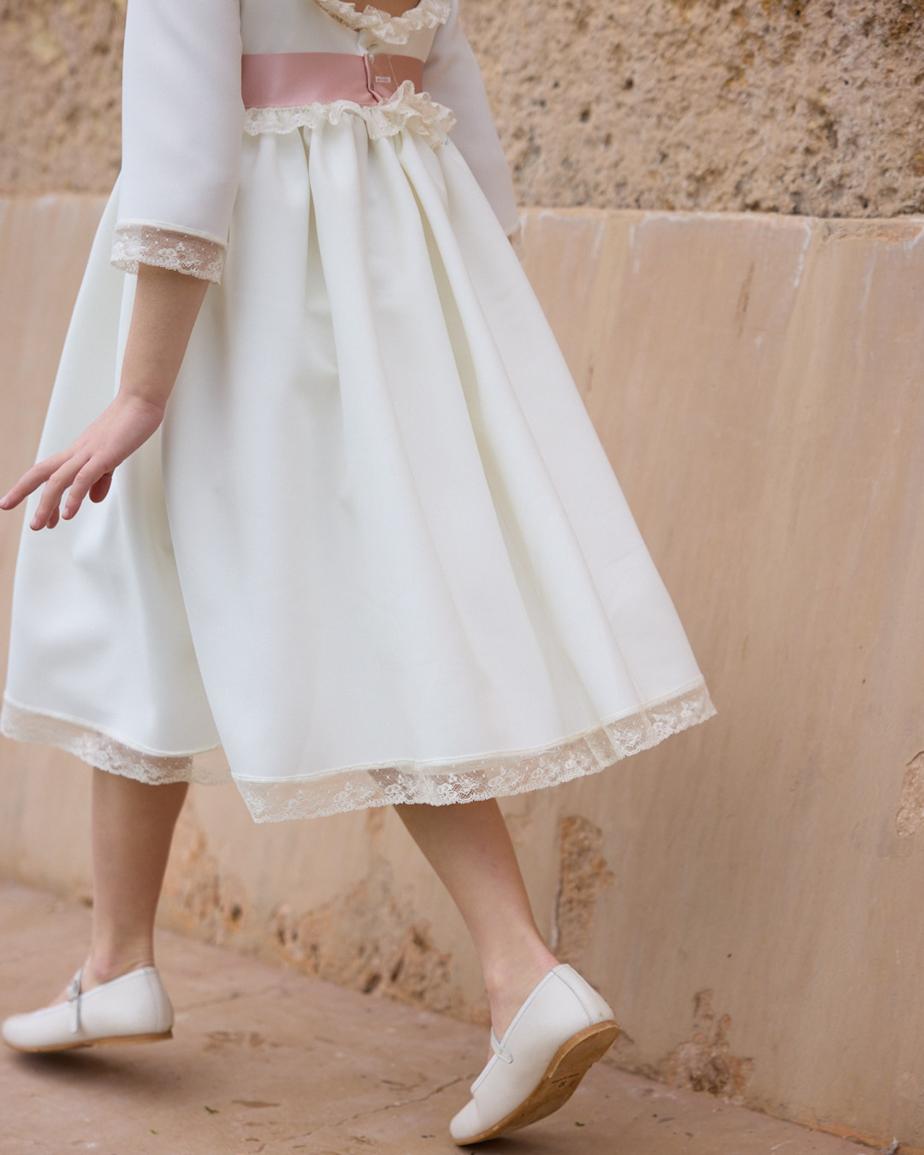 White dress with lace details worn by a person against a beige wall.