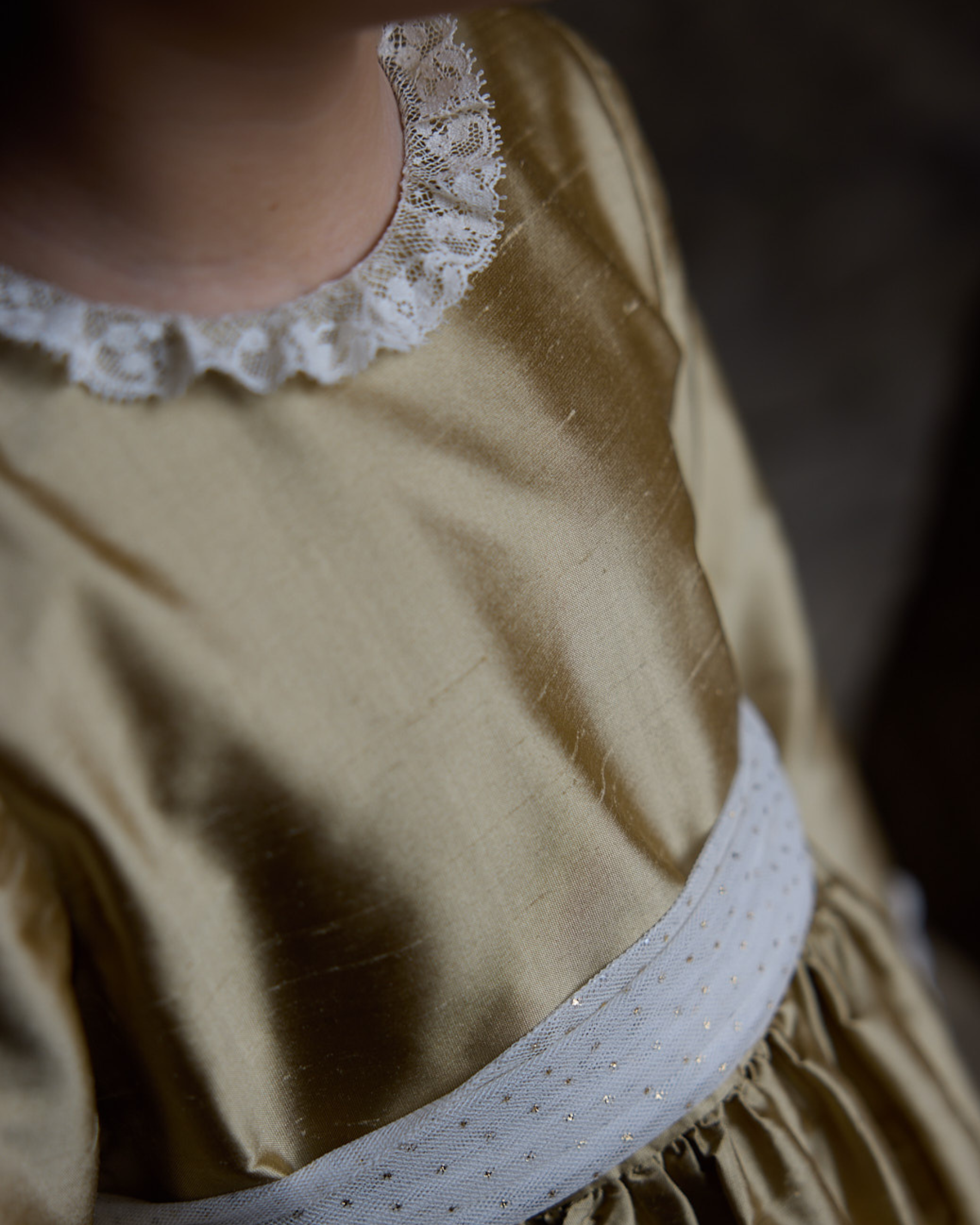 Close-up of a person wearing a beige dress with a lace collar and white belt.