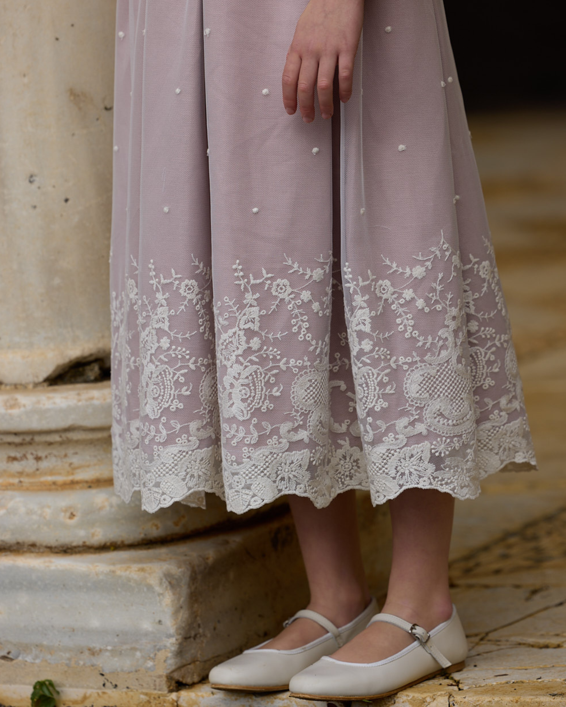 Person wearing a light purple dress with lace details standing on stone steps.