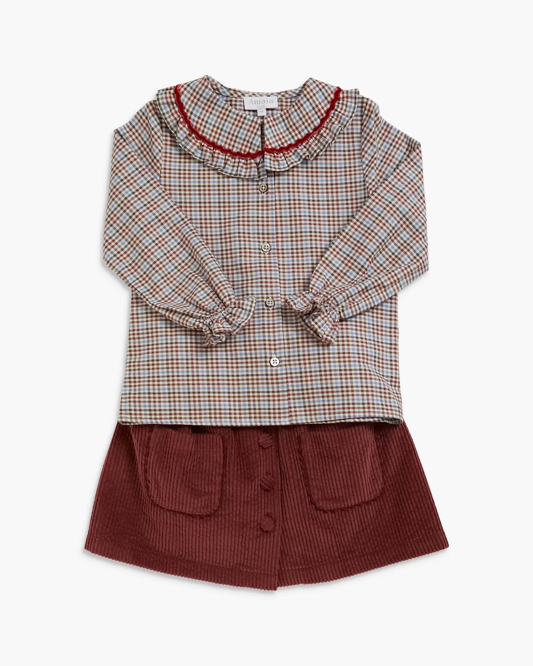 A children's two-piece outfit featuring a long-sleeve button-front top with a beige, brown, and red plaid pattern and a dark red ruffled collar, paired with a dark brown corduroy skirt with front pockets.