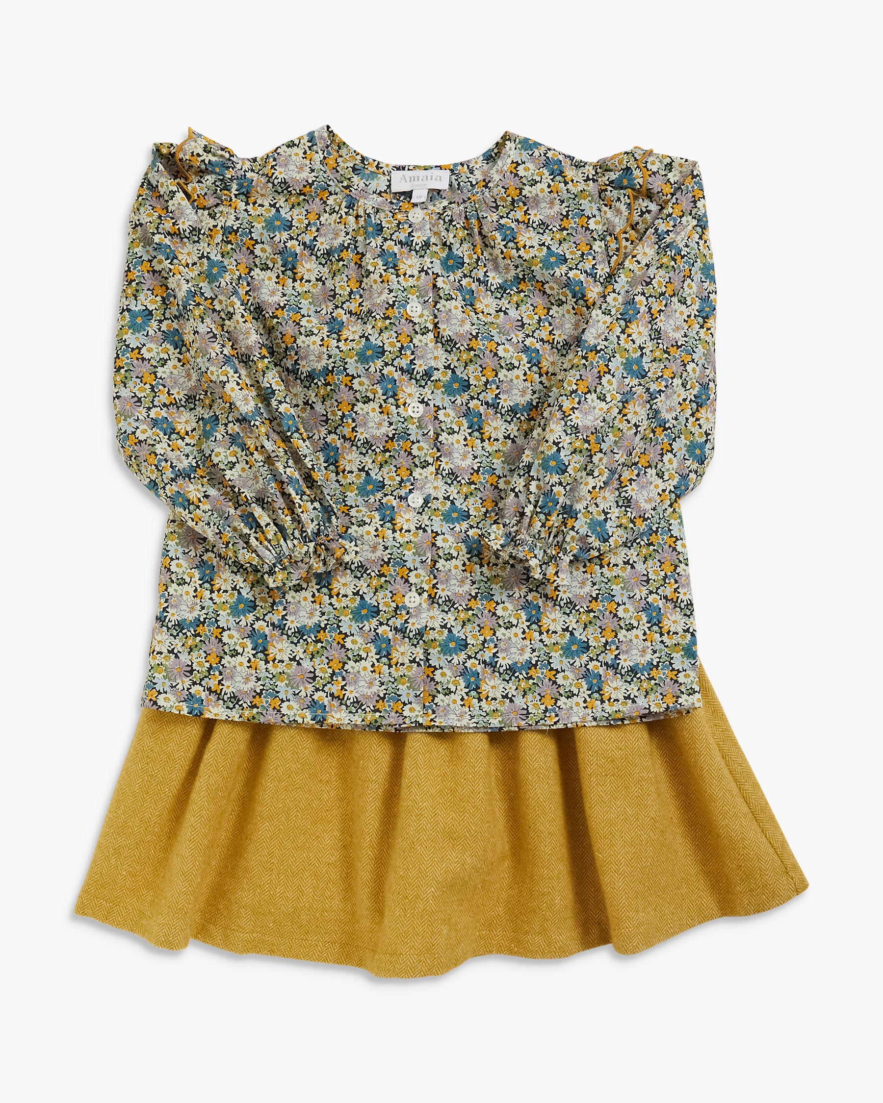 A children's long-sleeve blouse with a dense floral print in blue, yellow, and white over a solid mustard yellow flared skirt, shown flat on a light gray background.