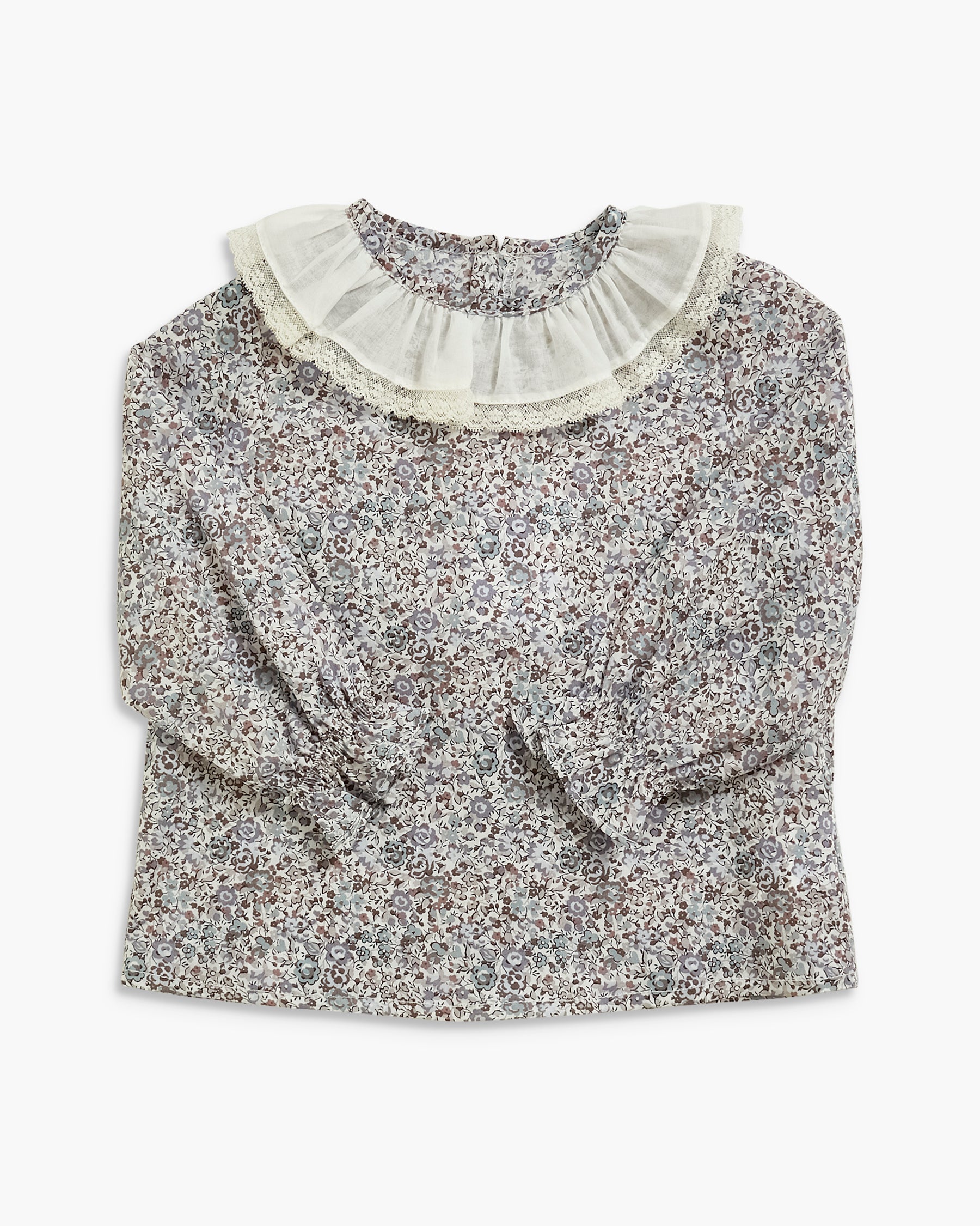A long-sleeve blouse with a dense small floral print in gray, white, and black, featuring a large cream ruffled collar and ruffled cuffs, laid flat against a light gray background.