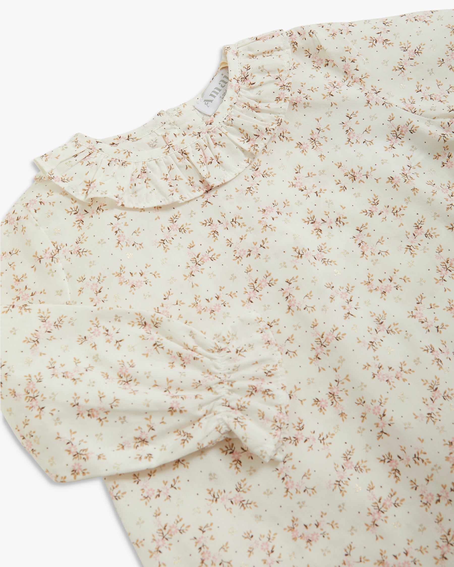 Close-up of a cream-colored blouse with a dense small floral print in muted brown and beige, featuring a ruffled collar and a gathered sleeve detail.