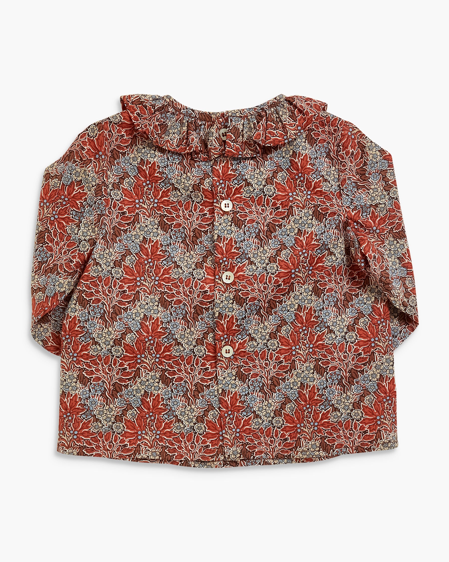 A long-sleeve button-up blouse with a ruffled collar, featuring an intricate floral and paisley pattern in red, brown, beige, and blue, laid flat against a light gray background.