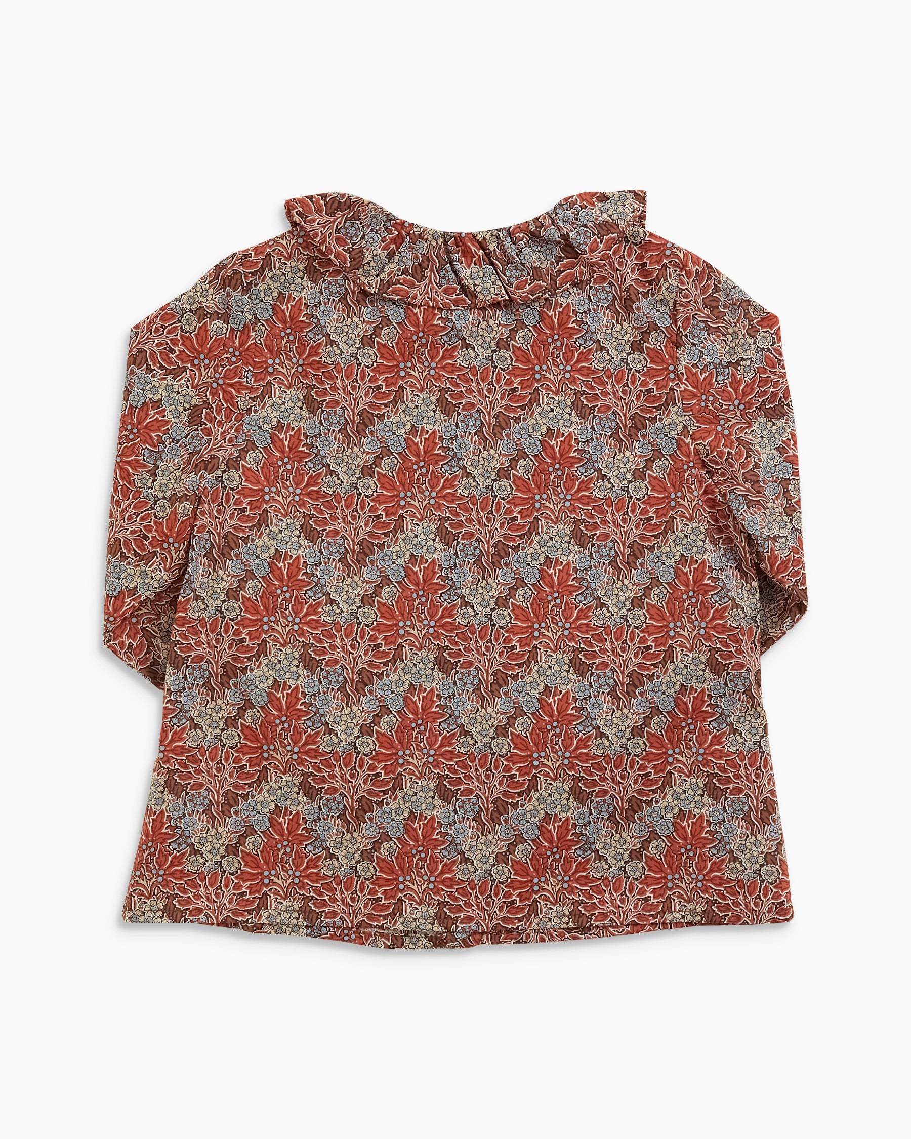 A long-sleeve blouse with a ruffled collar, featuring an intricate damask-style floral pattern in rust red, beige, and muted blue-gray tones, laid flat against a light gray background.