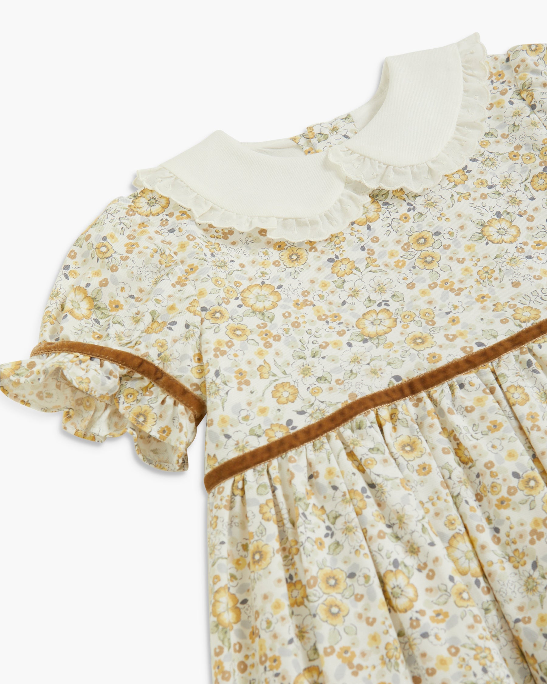 Close-up of a children's dress with a cream ruffled Peter Pan collar, a yellow and beige floral print, and a brown trim detail.