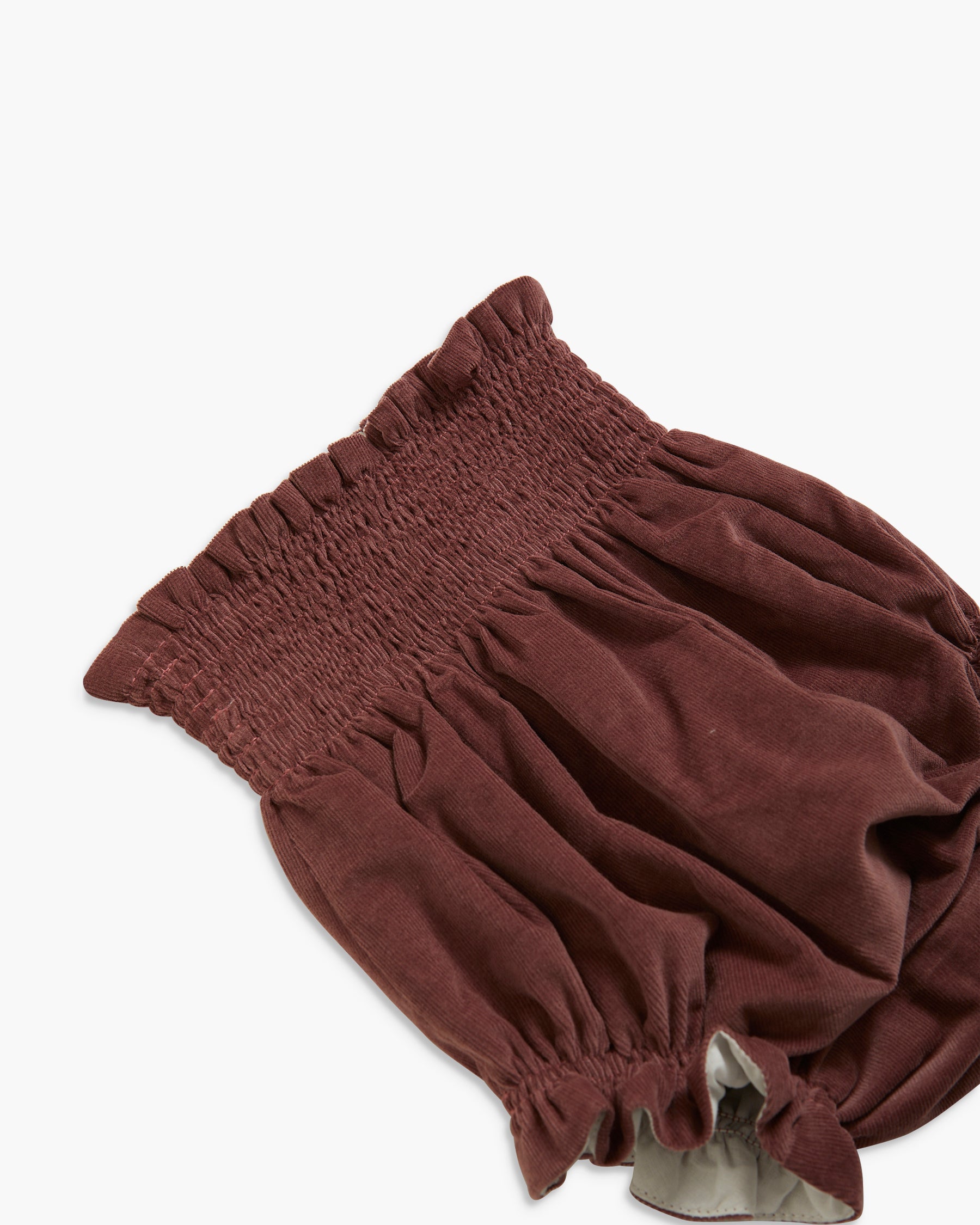A close-up of a dark brown fabric garment, likely a smocked bloomers or diaper cover, showing the elasticized waist and gathered legs on a plain white background.