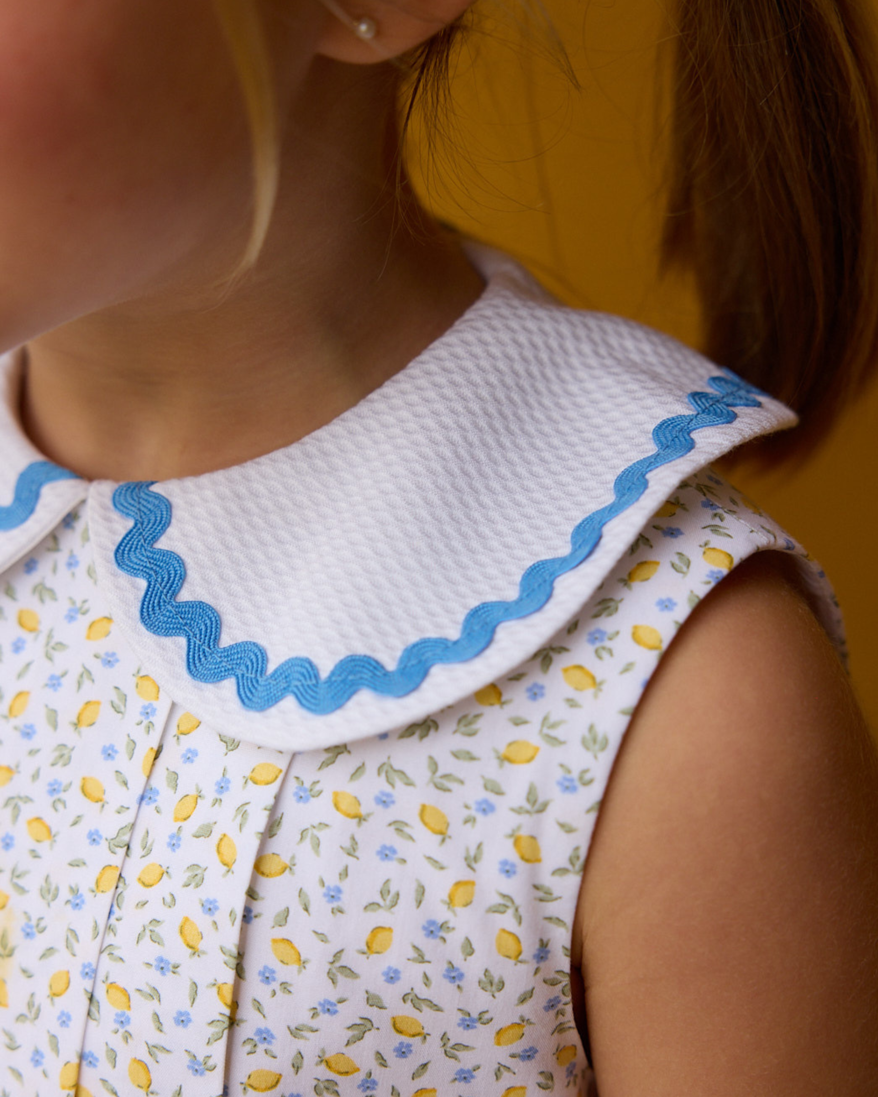 Close-up of a person wearing a dress with a white collar and blue trim, featuring a floral pattern.
