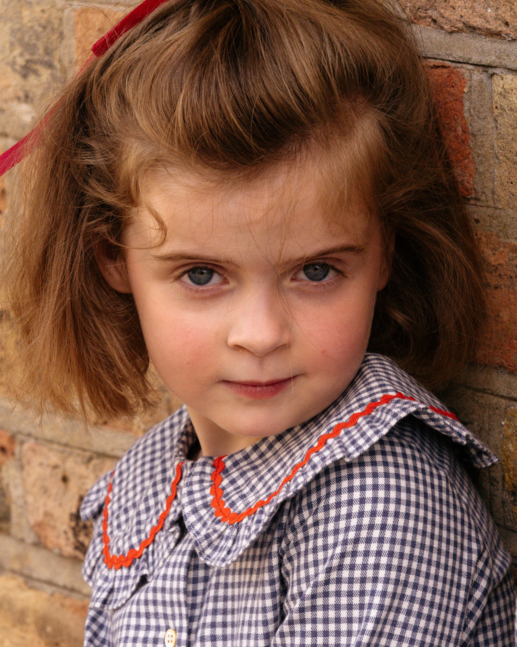 Young girl with a checkered dress against a brick wall