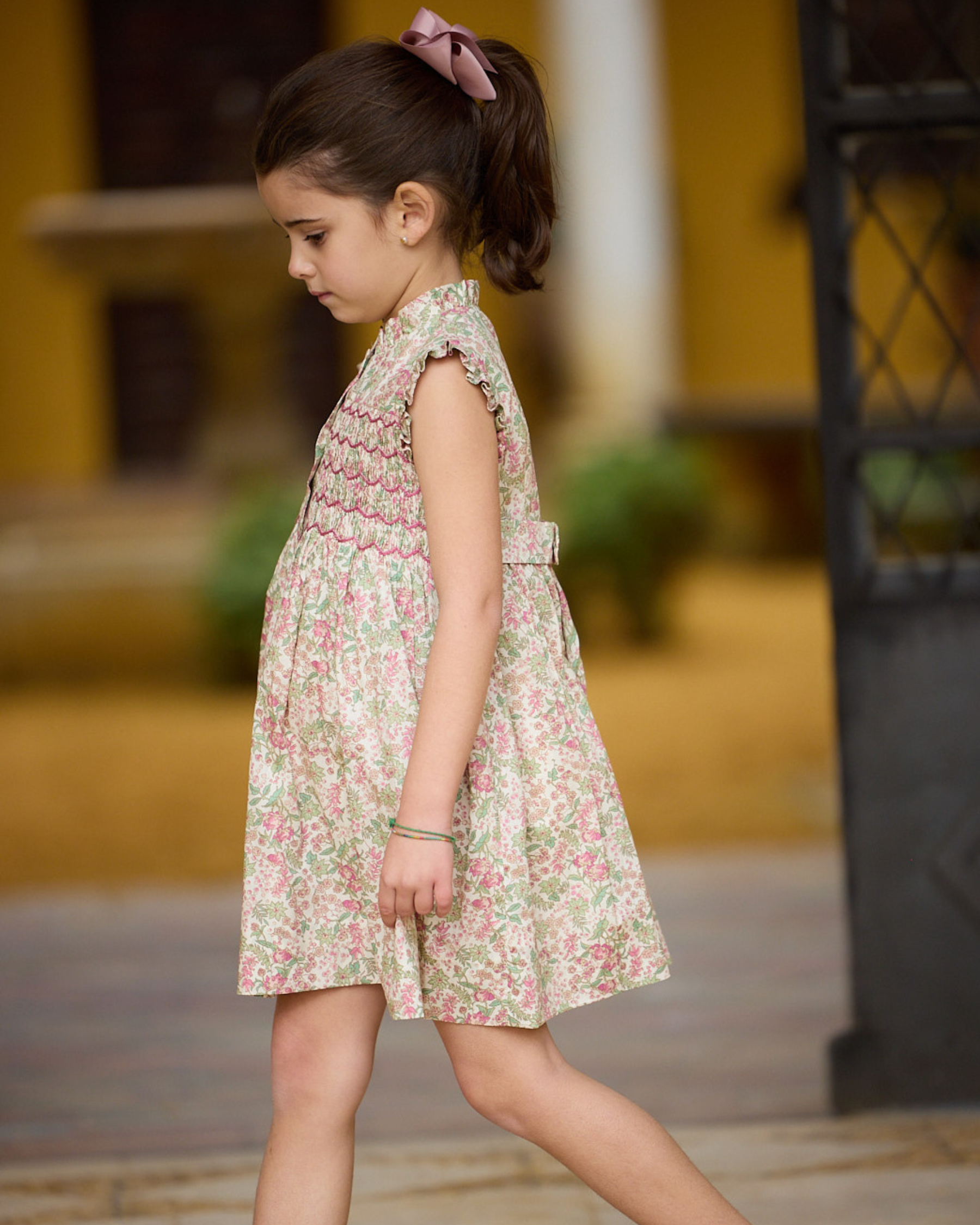 Young girl in a floral dress standing outdoors with a blurred background